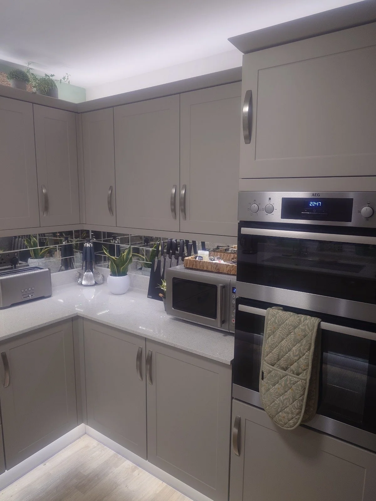 Modern kitchen with gray cabinets, built-in oven, microwave, cutting board, toaster, plants, and utensils on a countertop.