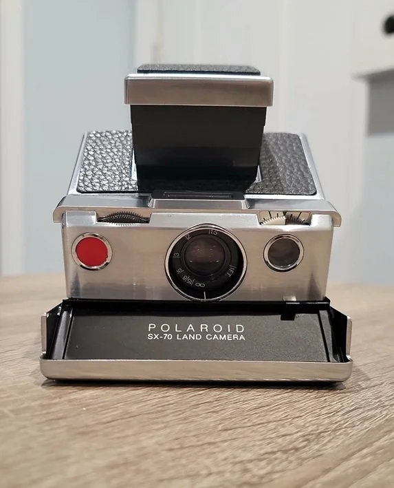 Refurbished silver and black Polaroid SX-70 Folding Land Camera with SX70R PCB, PolaVolt i-type adapter, and Aki Asahi replacement skin