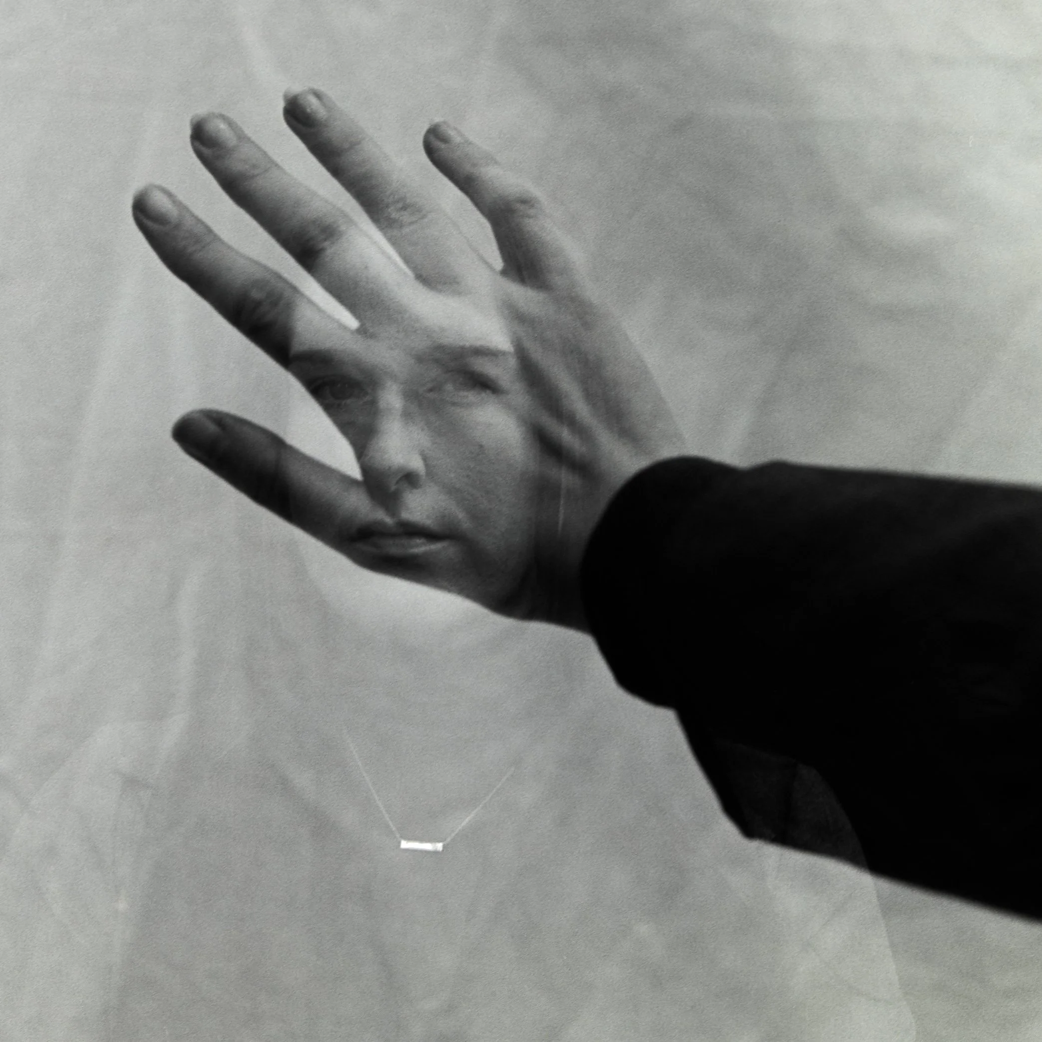 A person holds up their hand in front of their face, creating a layered visual effect with a black-and-white photograph of a woman’s face behind their hand.