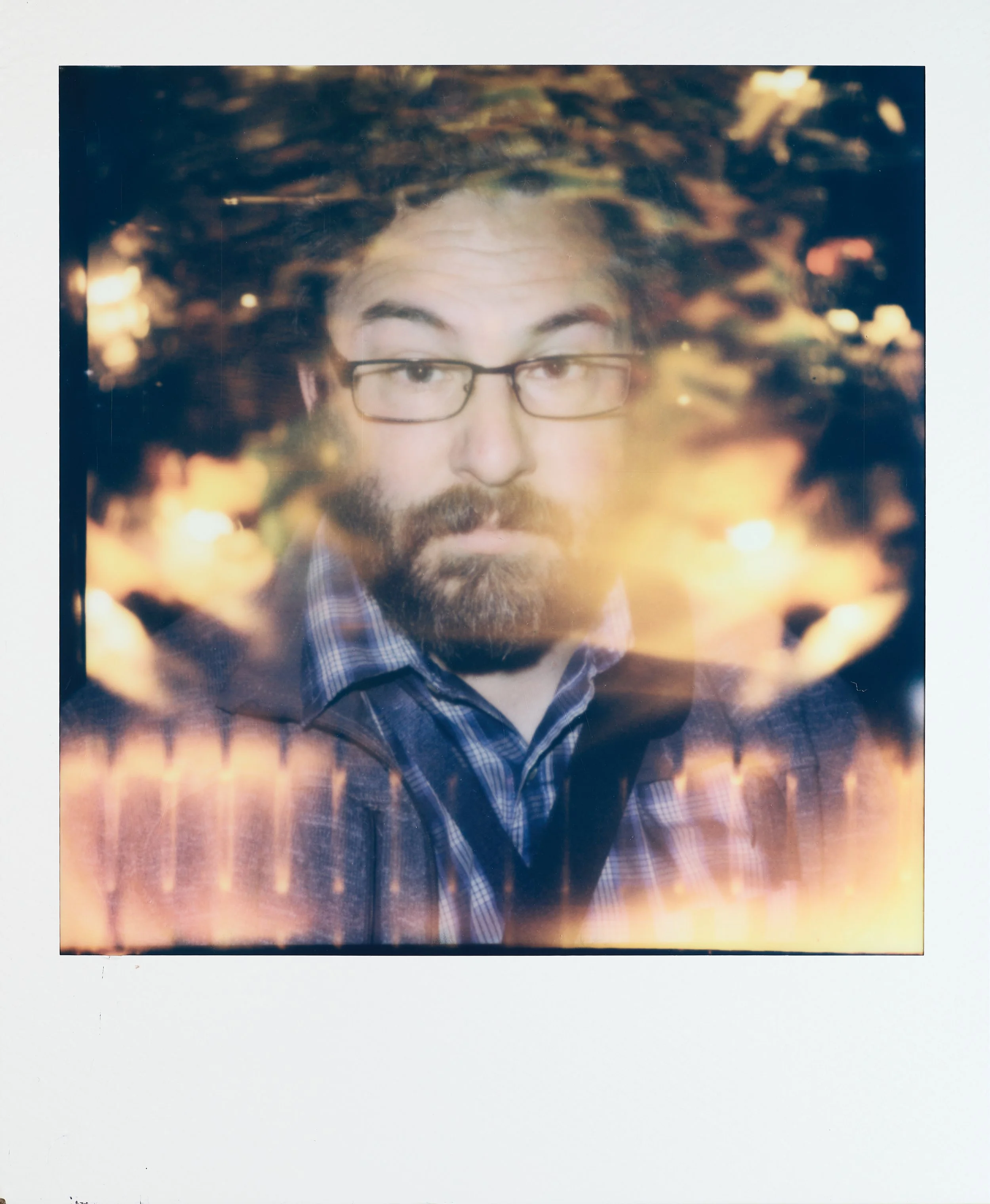 A portrait of a man with glasses, a beard, and a mustache, wearing a checkered shirt, with an artistic overlay of blurred lights.