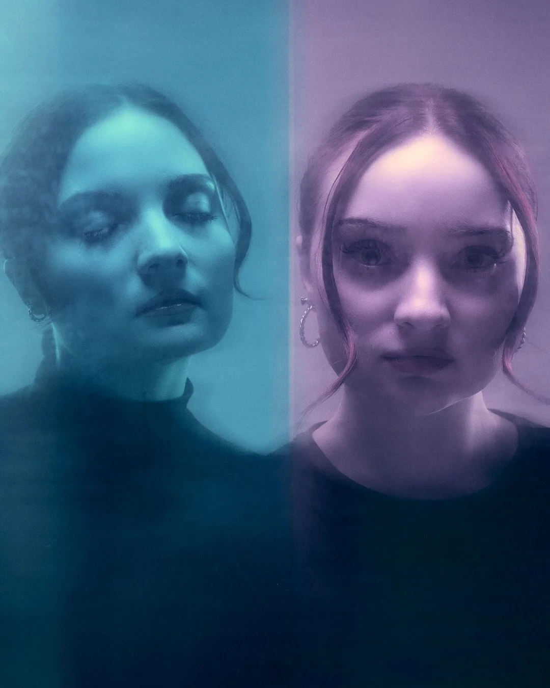 Two women with short hair and earrings face a camera through translucent, colored glass, one with closed eyes and the other with open eyes.