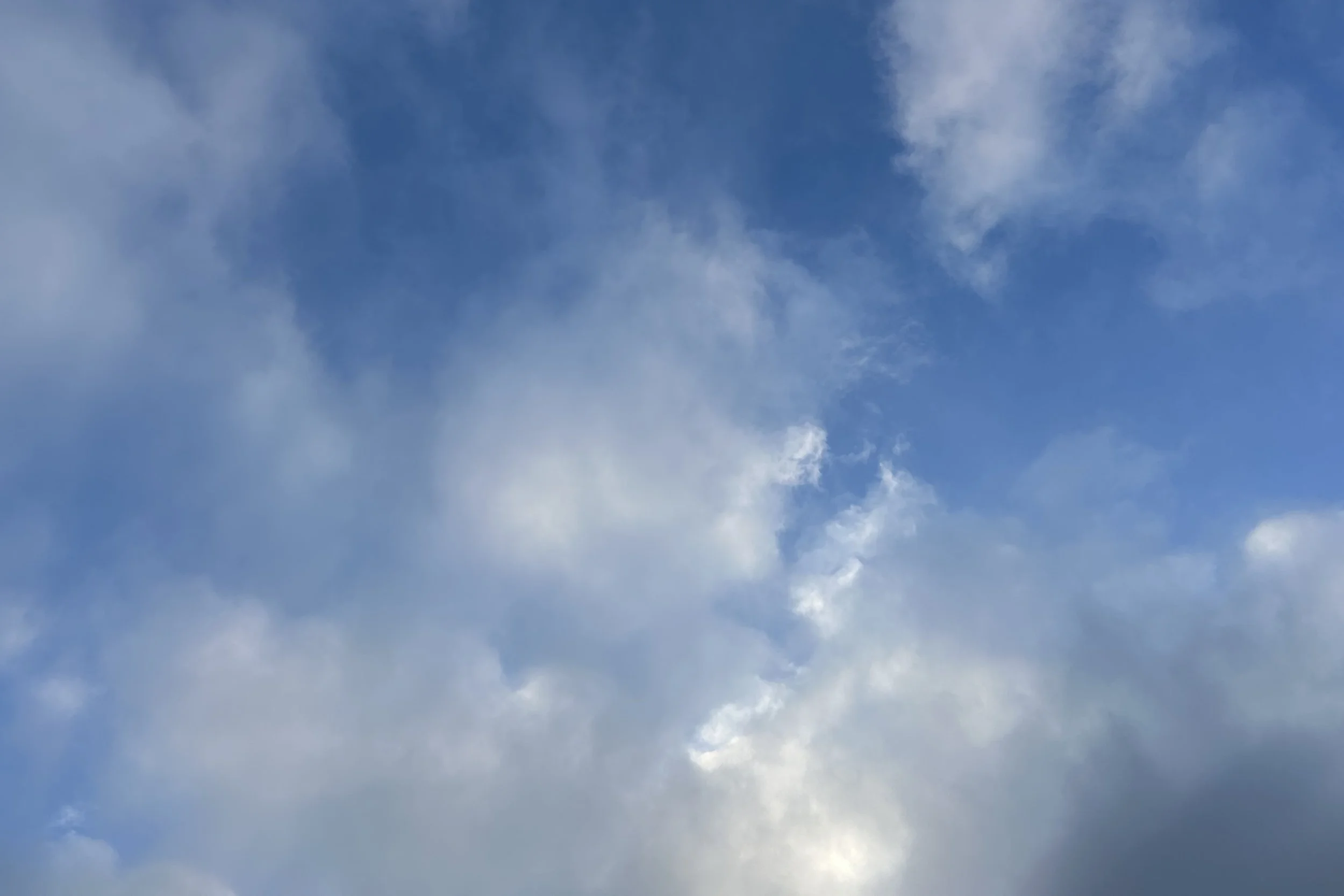 Layers of white and grey clouds with patches of blue sky, light breaking through at the centre