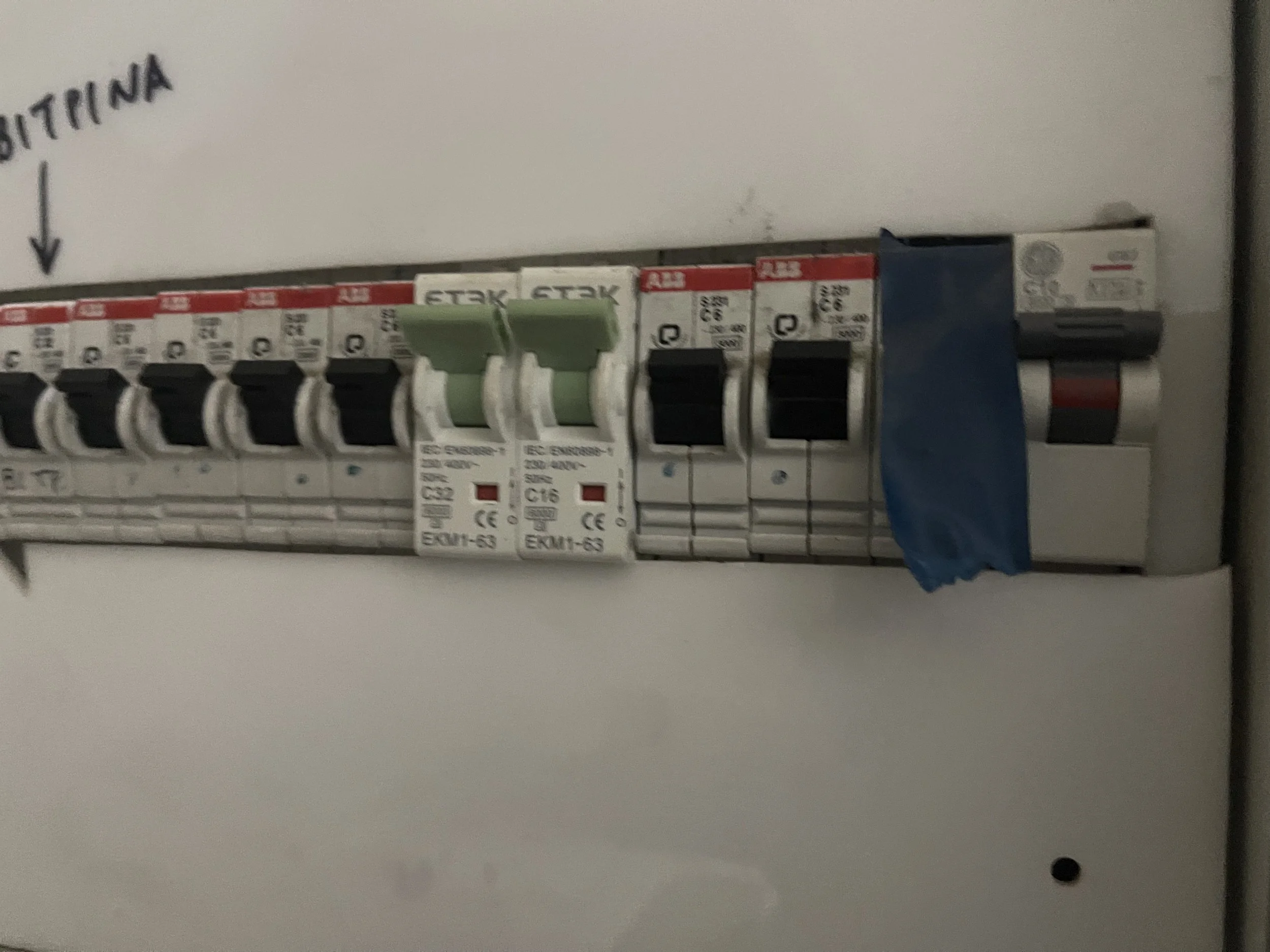 A close-up of an electrical circuit breaker panel with several circuit breakers installed, including green, black, and gray switches, mounted on a white background.