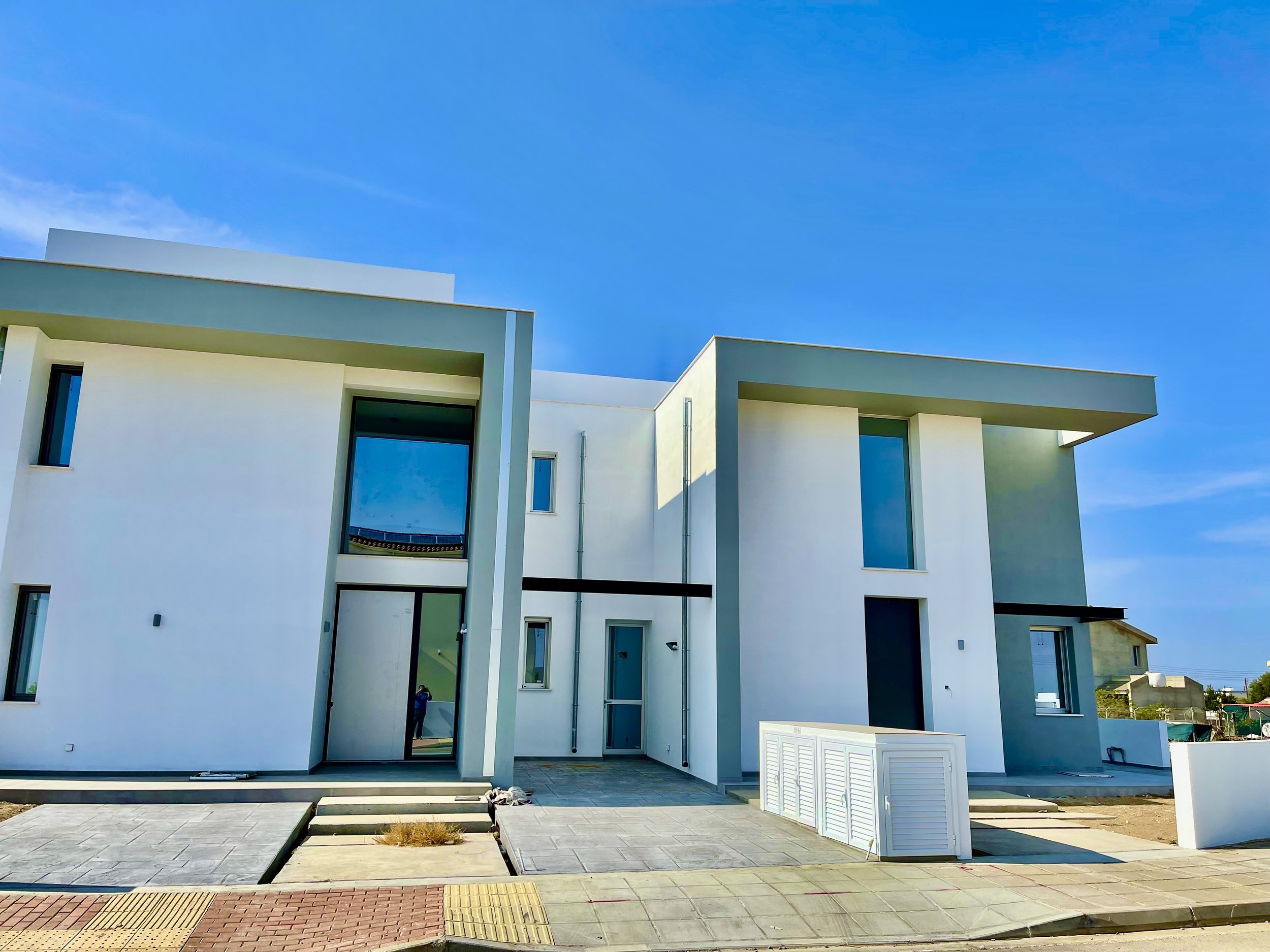 Modern white residential building with large windows and flat roof, under a clear blue sky.