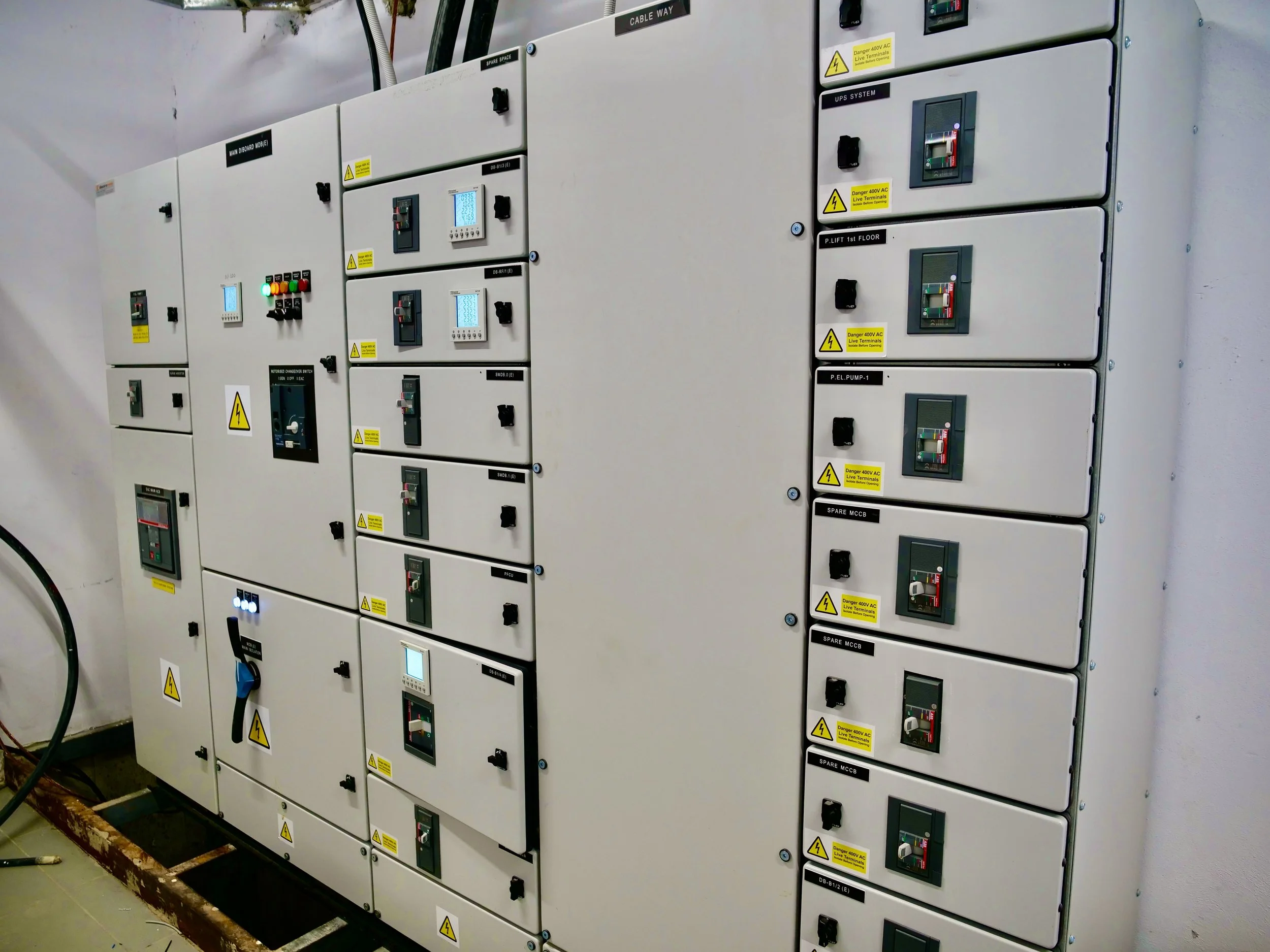 Electrical control panels with warning labels, switches, and digital displays mounted on a wall in an industrial setting.