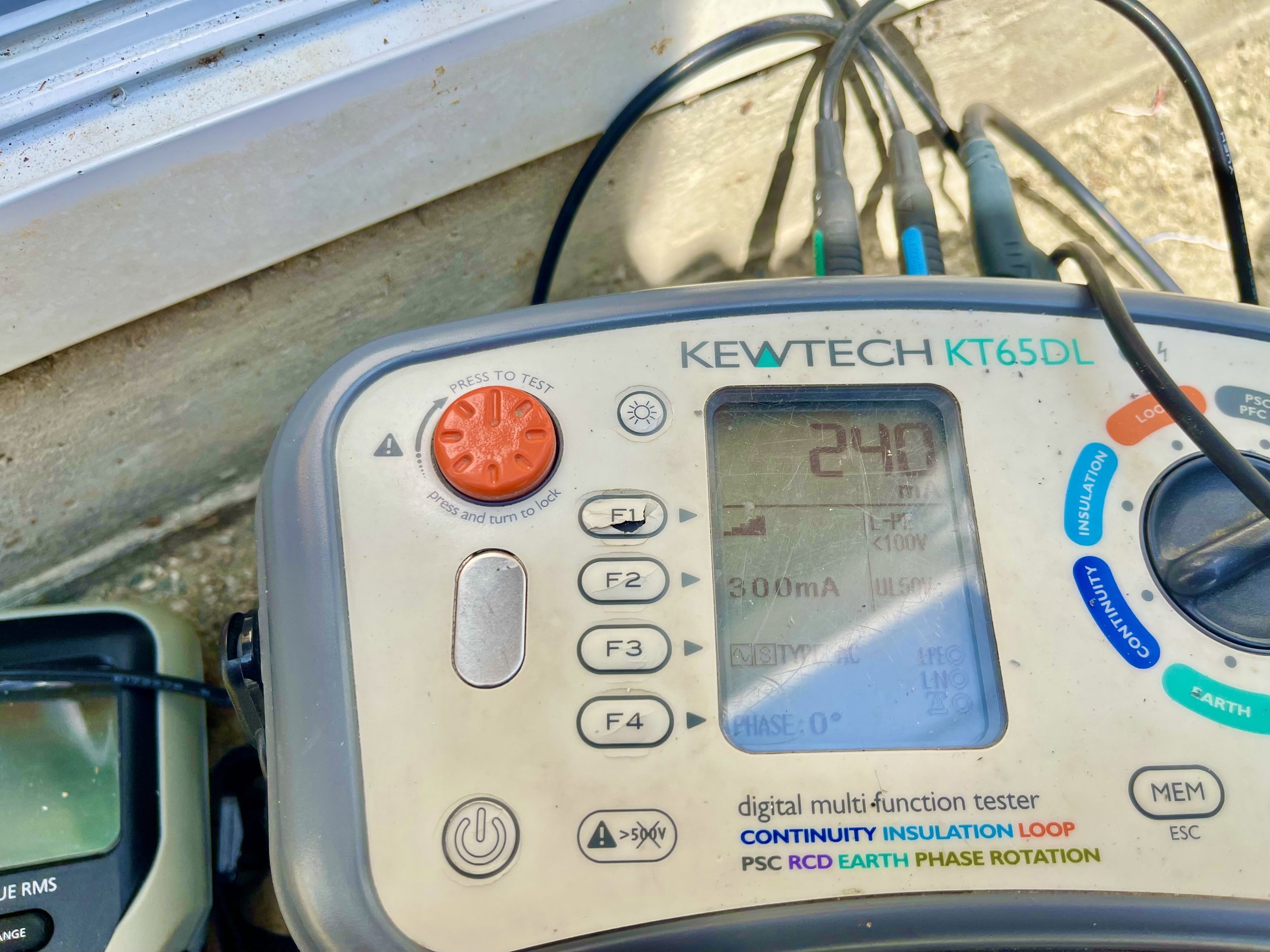 A digital multi-function tester device with cables connected to it, displaying a screen with the number 240. The device is labeled KEWTECH KT65DL and has various buttons and color-coded labels for testing and insulation functions.