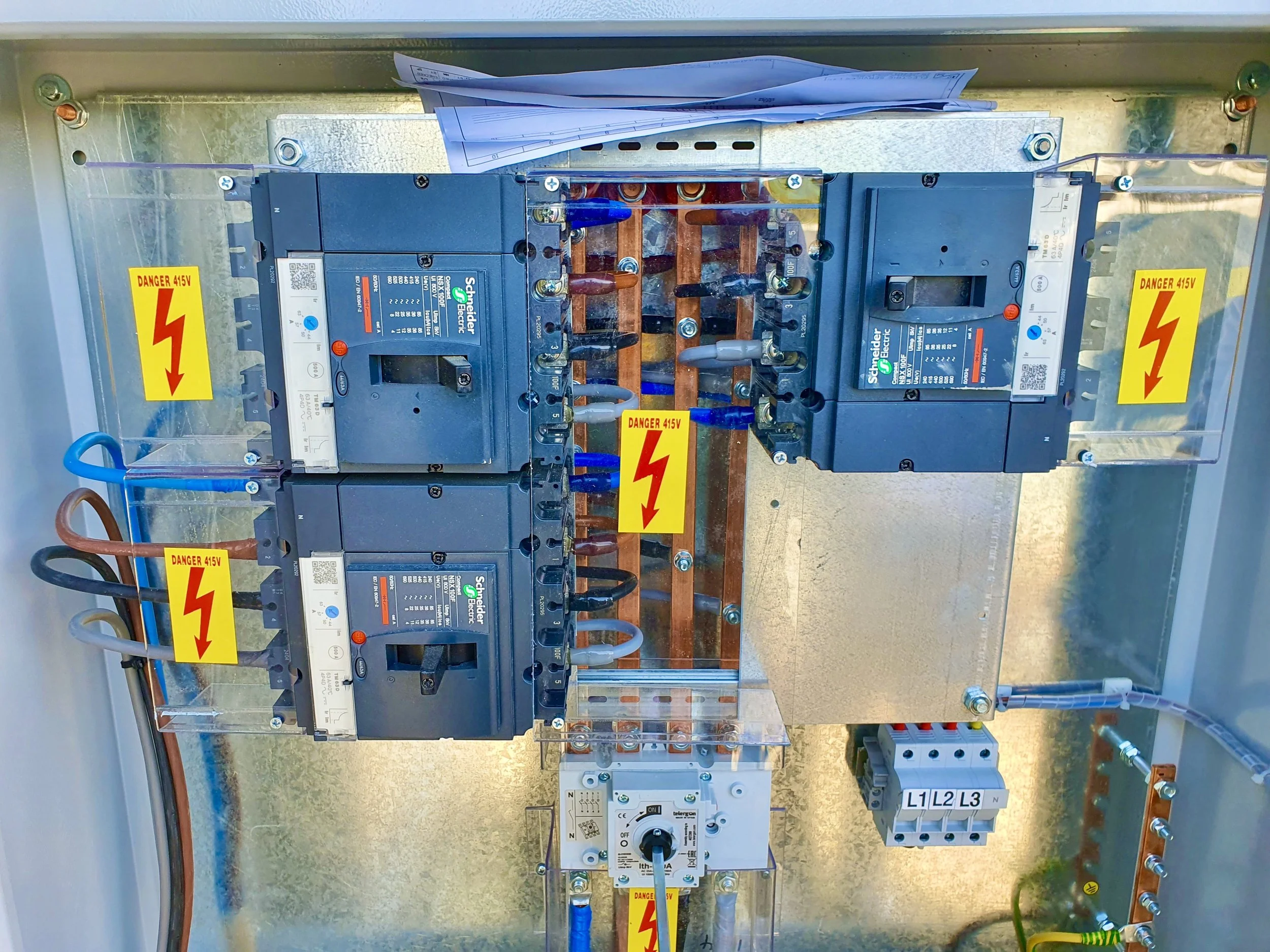 An electrical panel with circuit breakers connected by colored wires, labeled with danger signs warning of 415 volts.