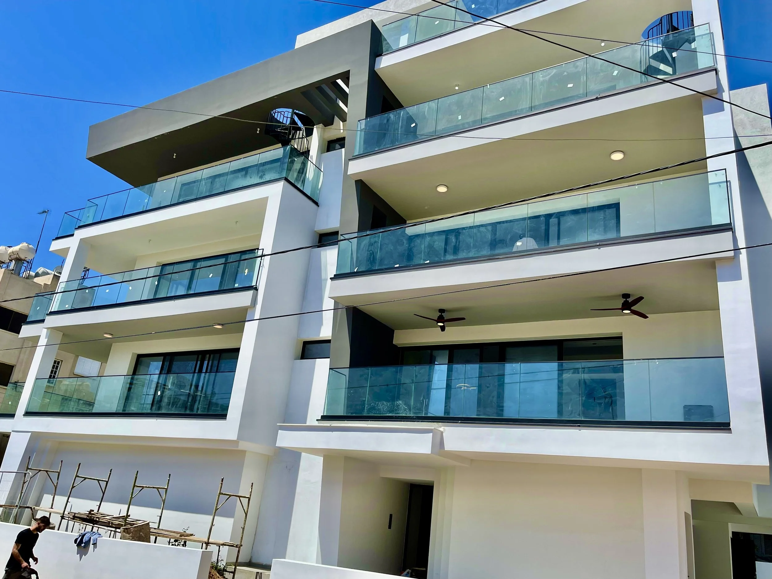 Modern multi-story apartment building with glass balconies and a clear blue sky