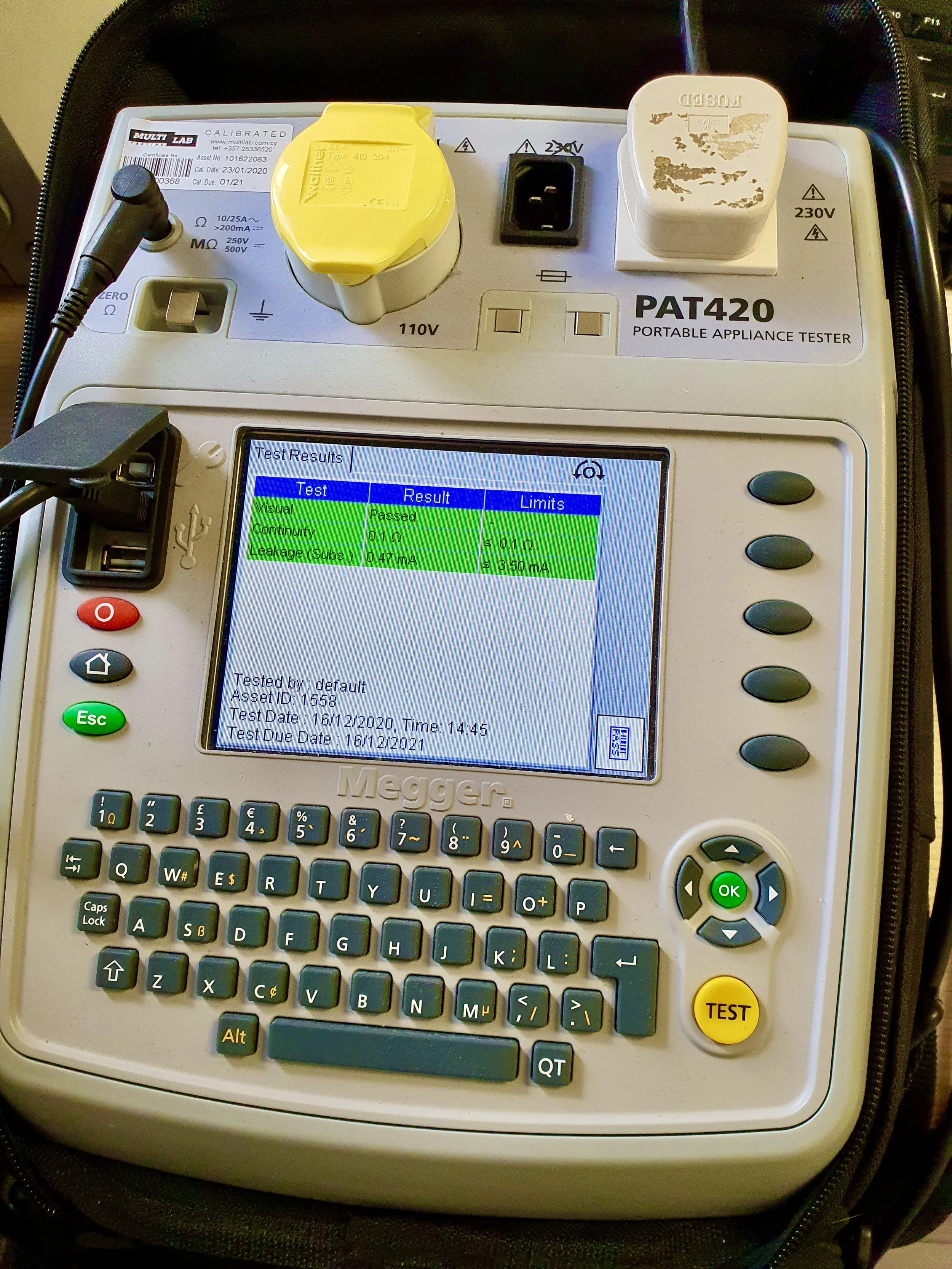 A portable appliance tester device with a computer screen displaying test results, a keyboard, and various plugs and sockets, used for testing electrical devices.