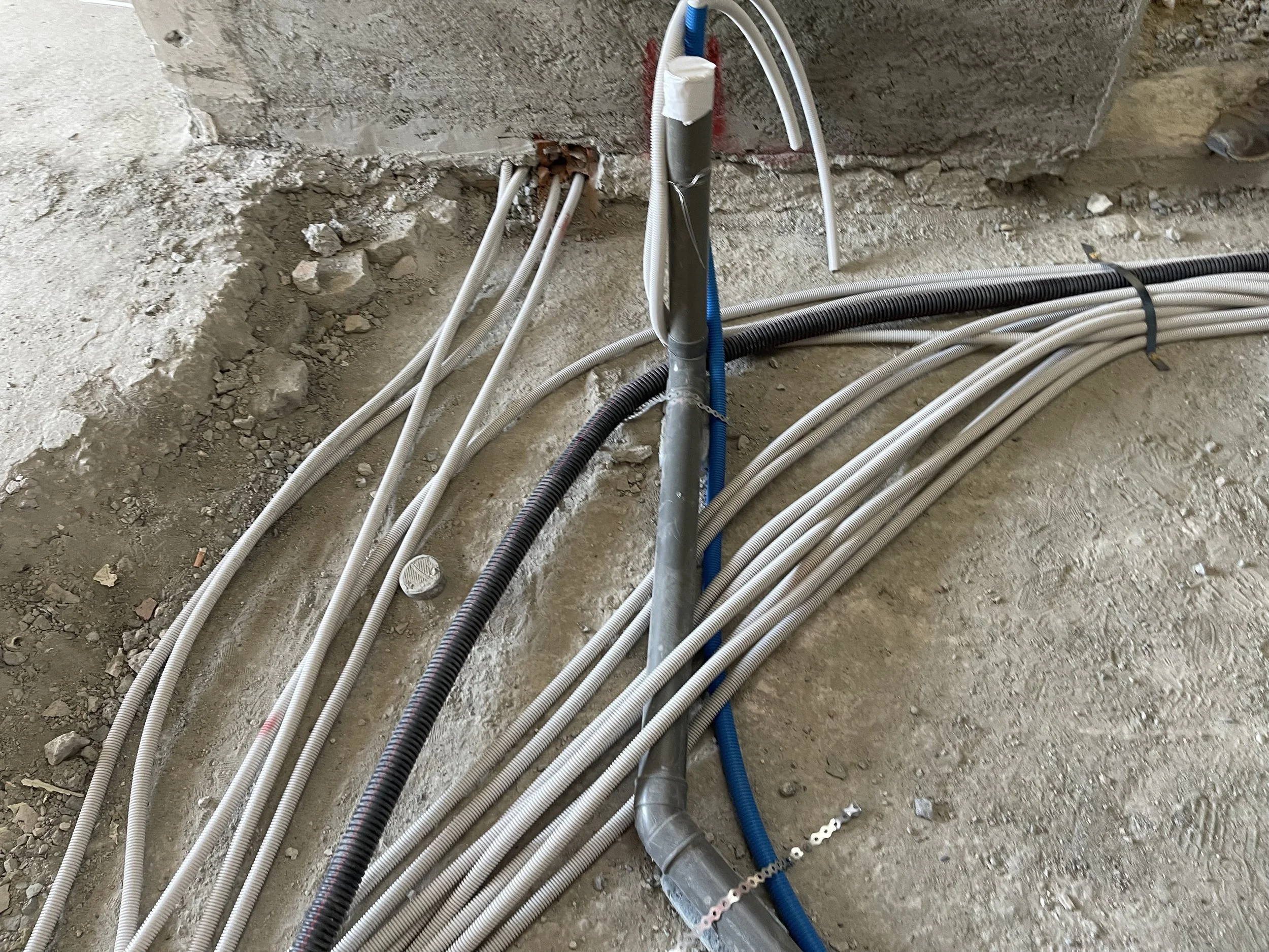 Various electrical conduits and cables installed on a rough concrete floor at a construction site.