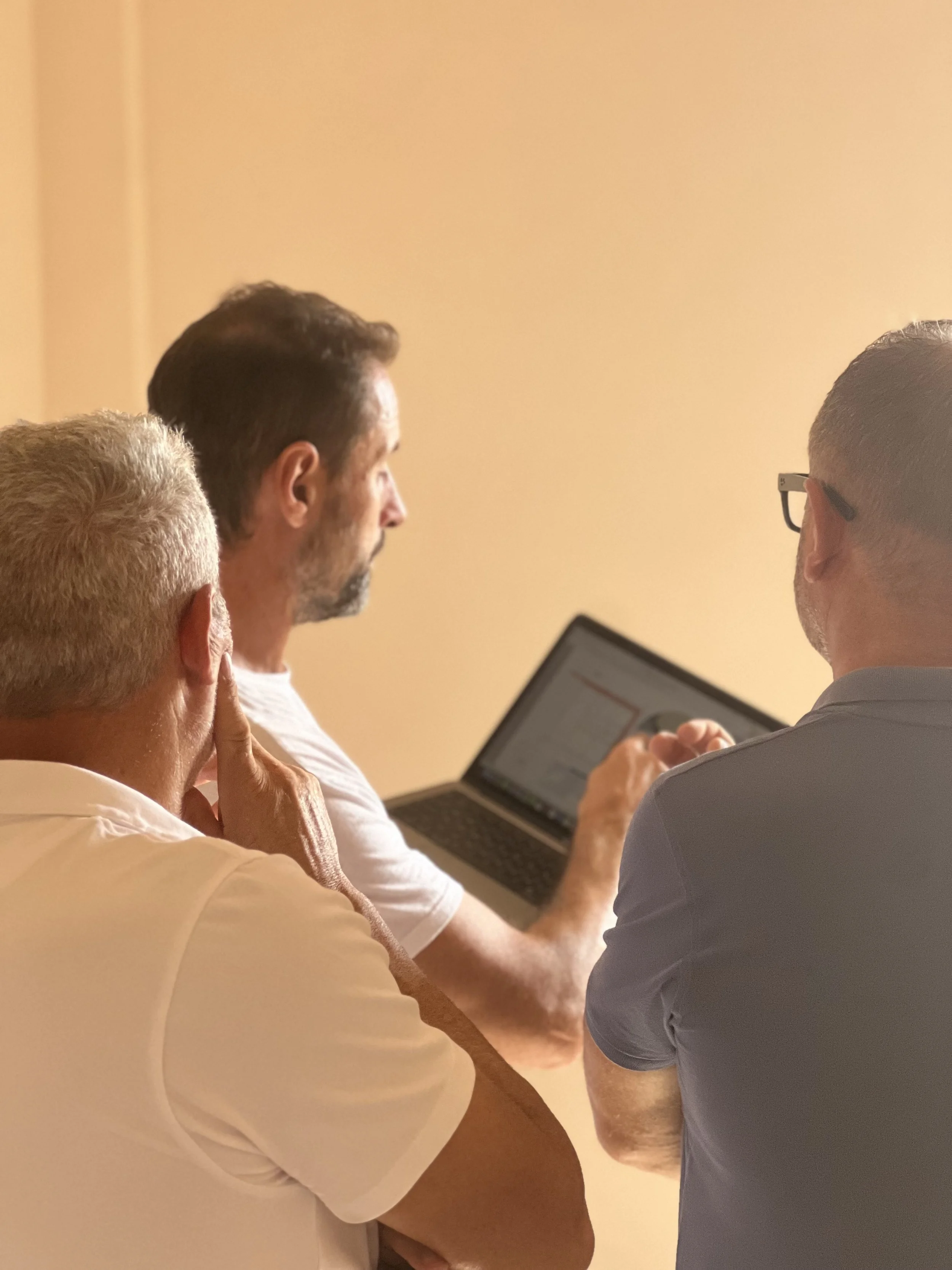 A modern living room with wooden floors, white walls, and a large sliding glass door leading to a balcony with outdoor furniture and a scenic view of the landscape.