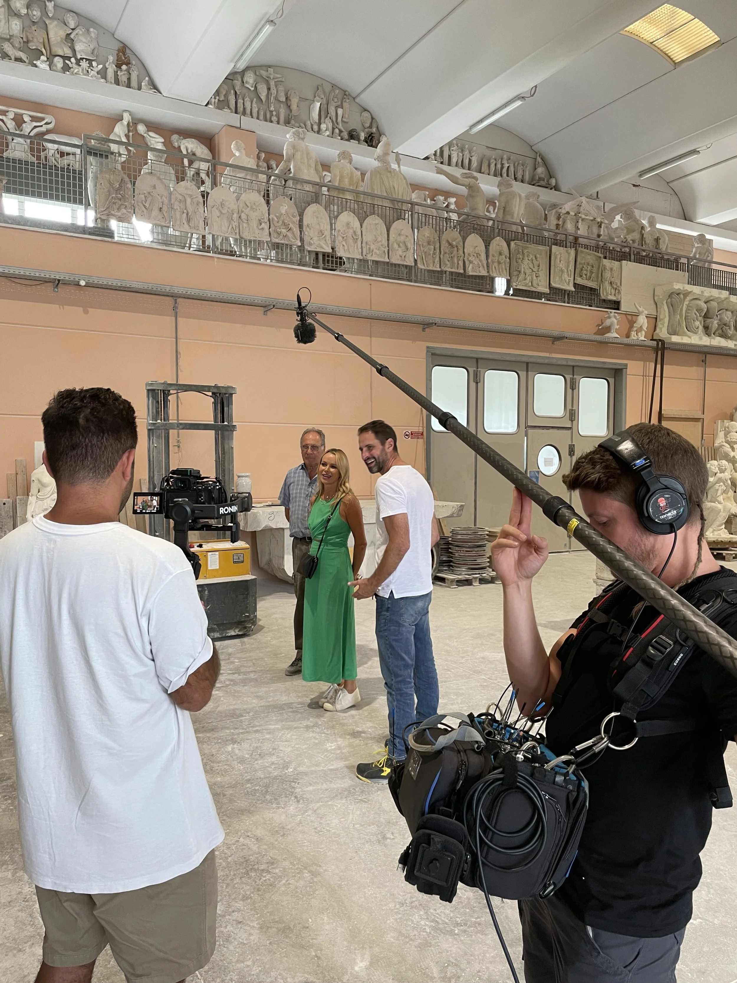 Television crew filming a conversation in a workshop filled with sculptural moulds