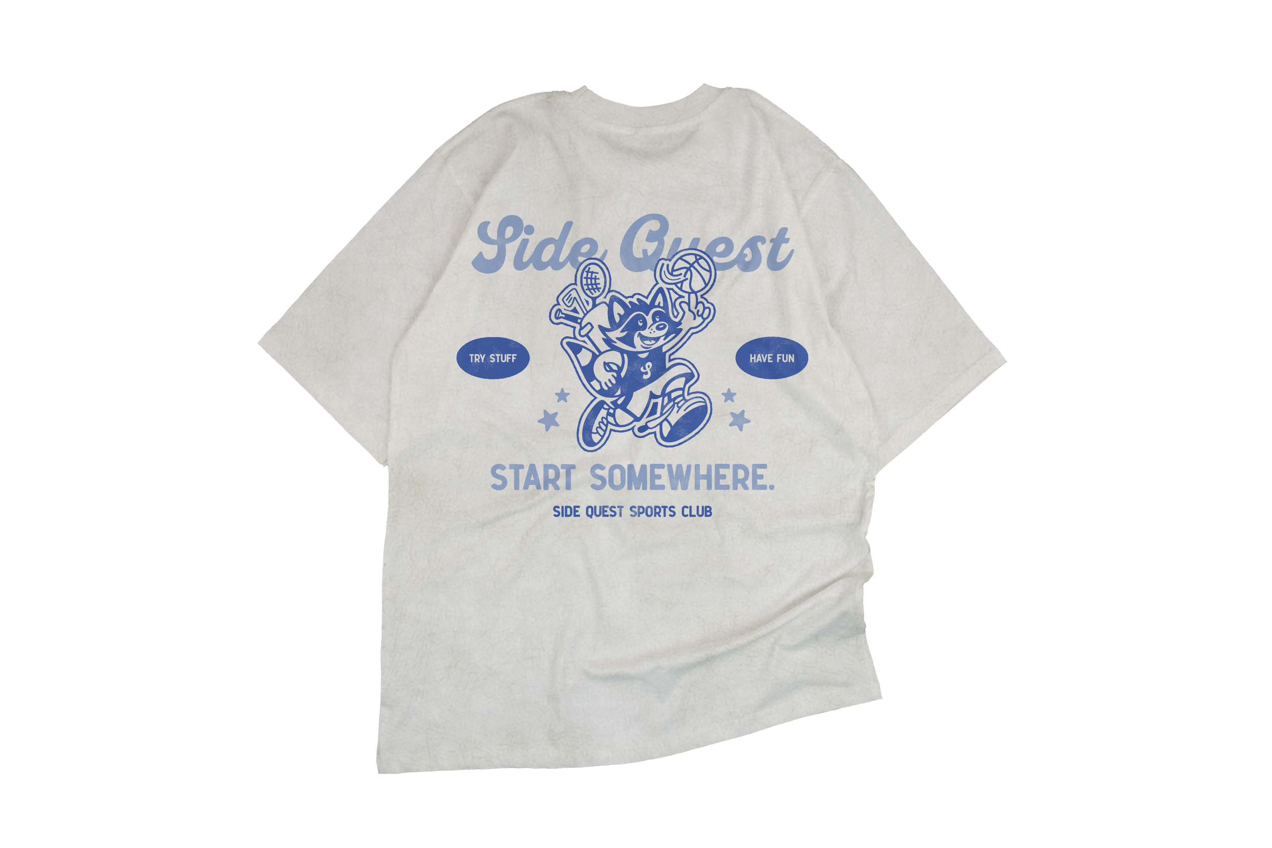 A white T-shirt with a blue graphic of a cartoon fox holding a tennis racket and a volleyball. The shirt has the phrase 'Side Quest' and the slogan 'Start Somewhere' printed on it, along with smaller phrases 'Try Stuff' and 'Have Fun', and the text 'Side Quest Sports Club'.
