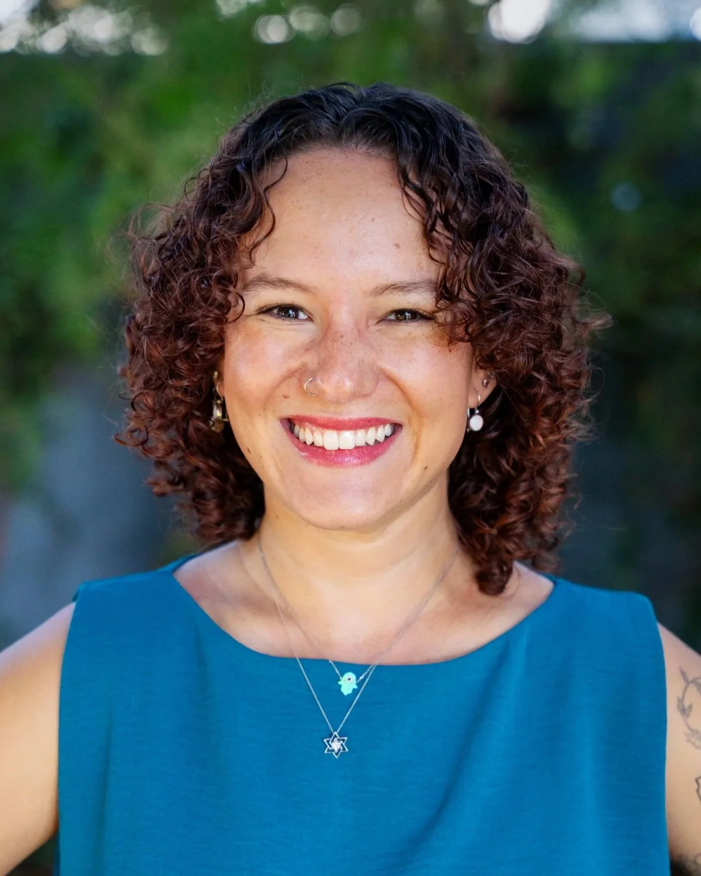 A smiling woman with curly hair standing on a beach during sunset.