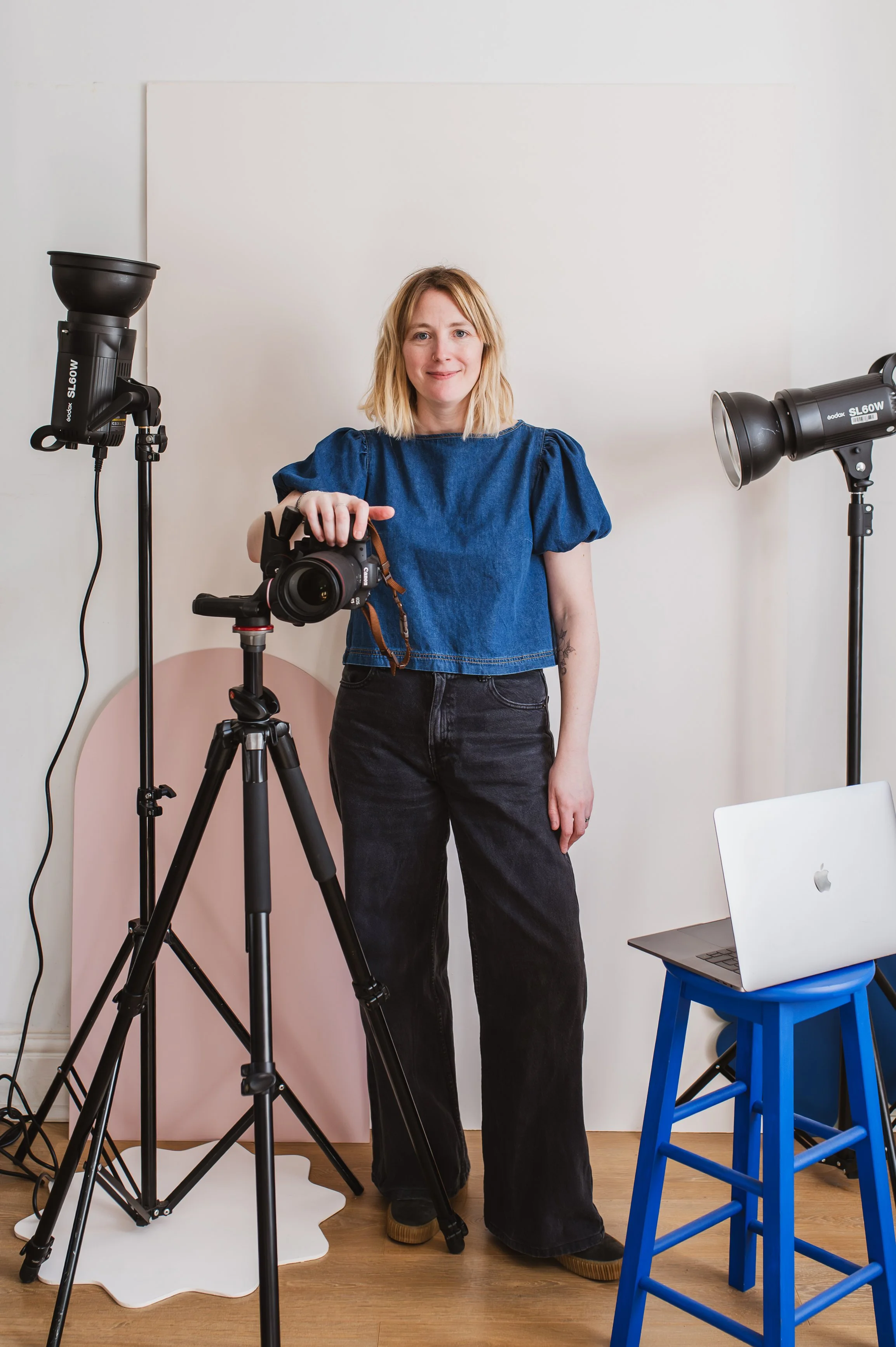  Faye Hedges brand shoot behind the scenes. Lady with blonde hair and wearing blue top and dark trousers standing next to her camera. 