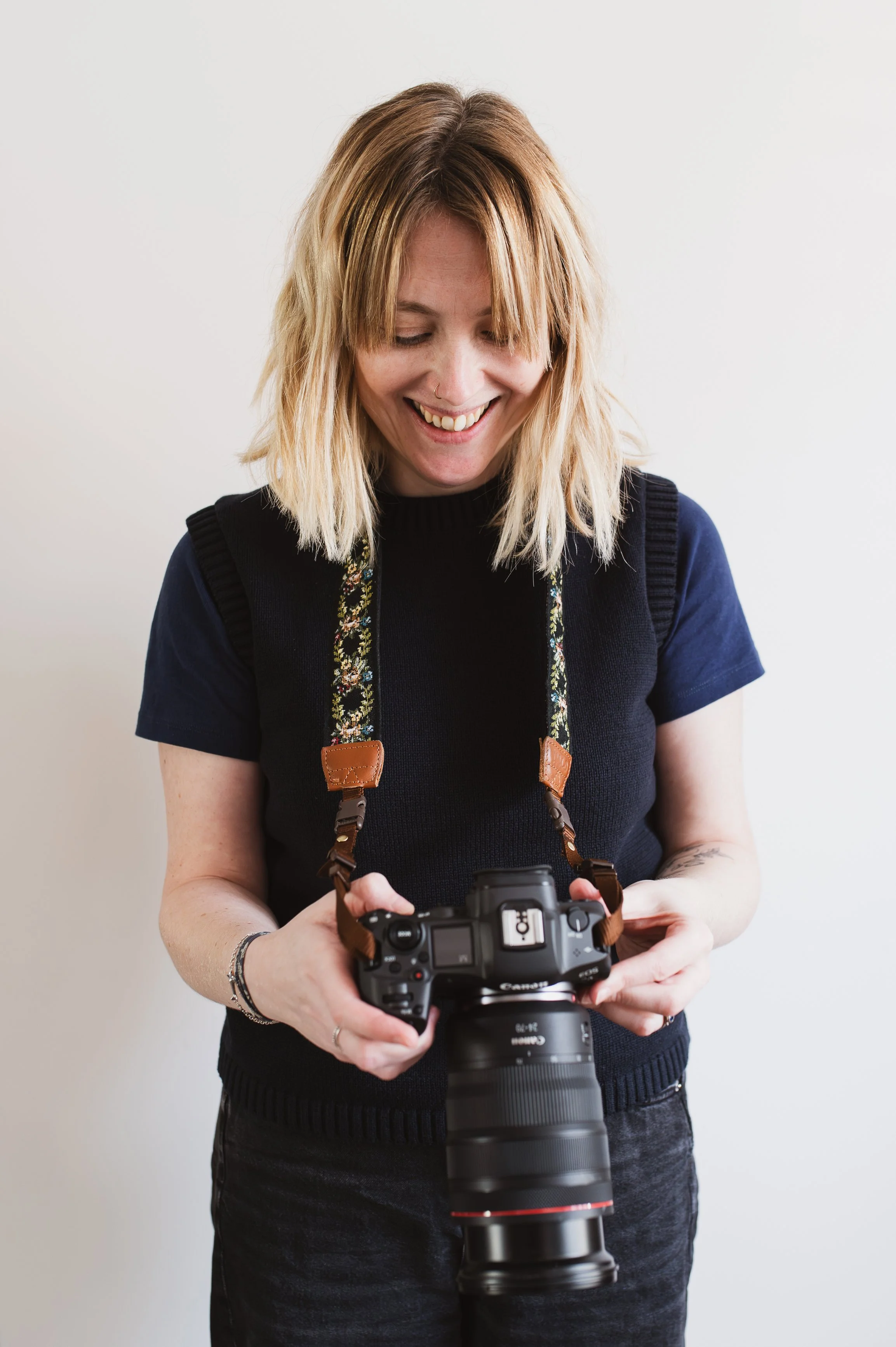 Lady with blonde hair smiling and looking down at her camera. The camera strap is around her neck. 