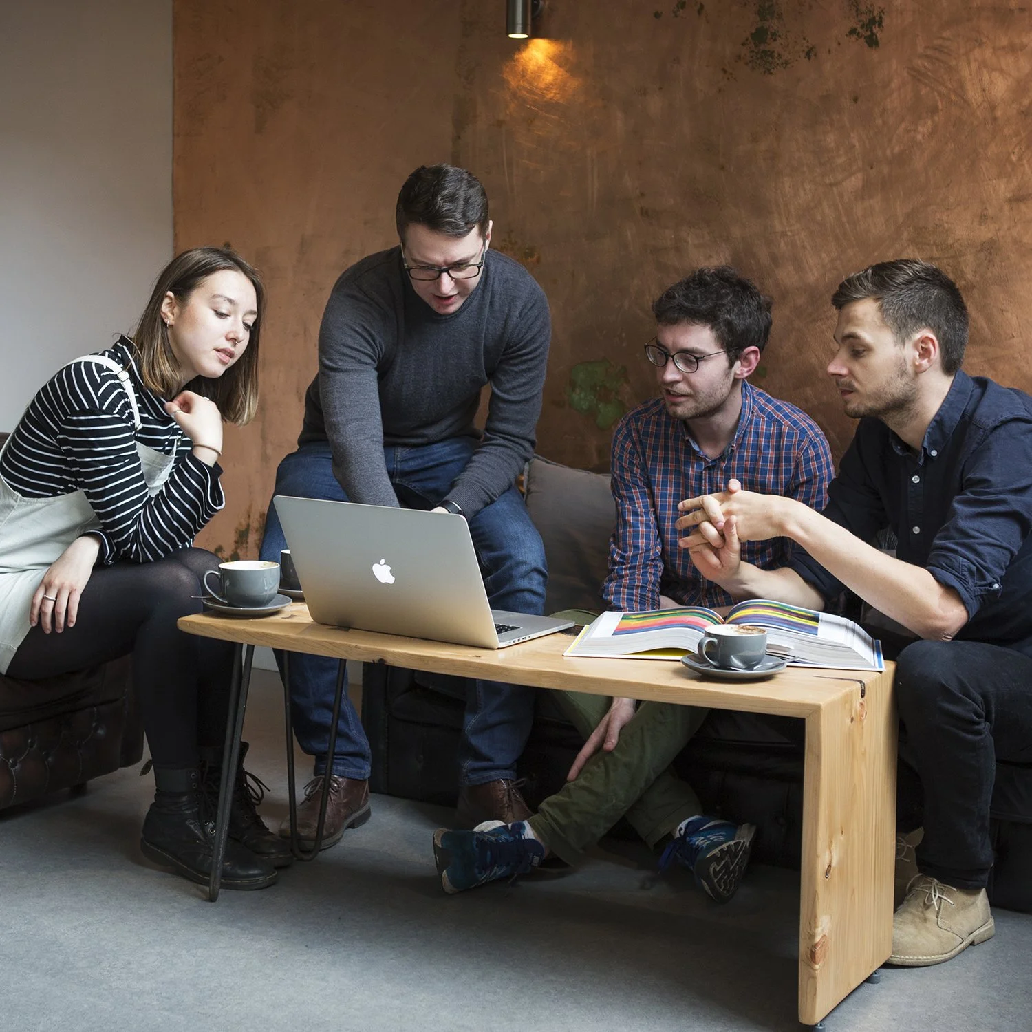 Brand photo of Bristol business meeting. Four young adults gathered around a laptop on a wooden table in a cozy room, engaged in a discussion or working together.