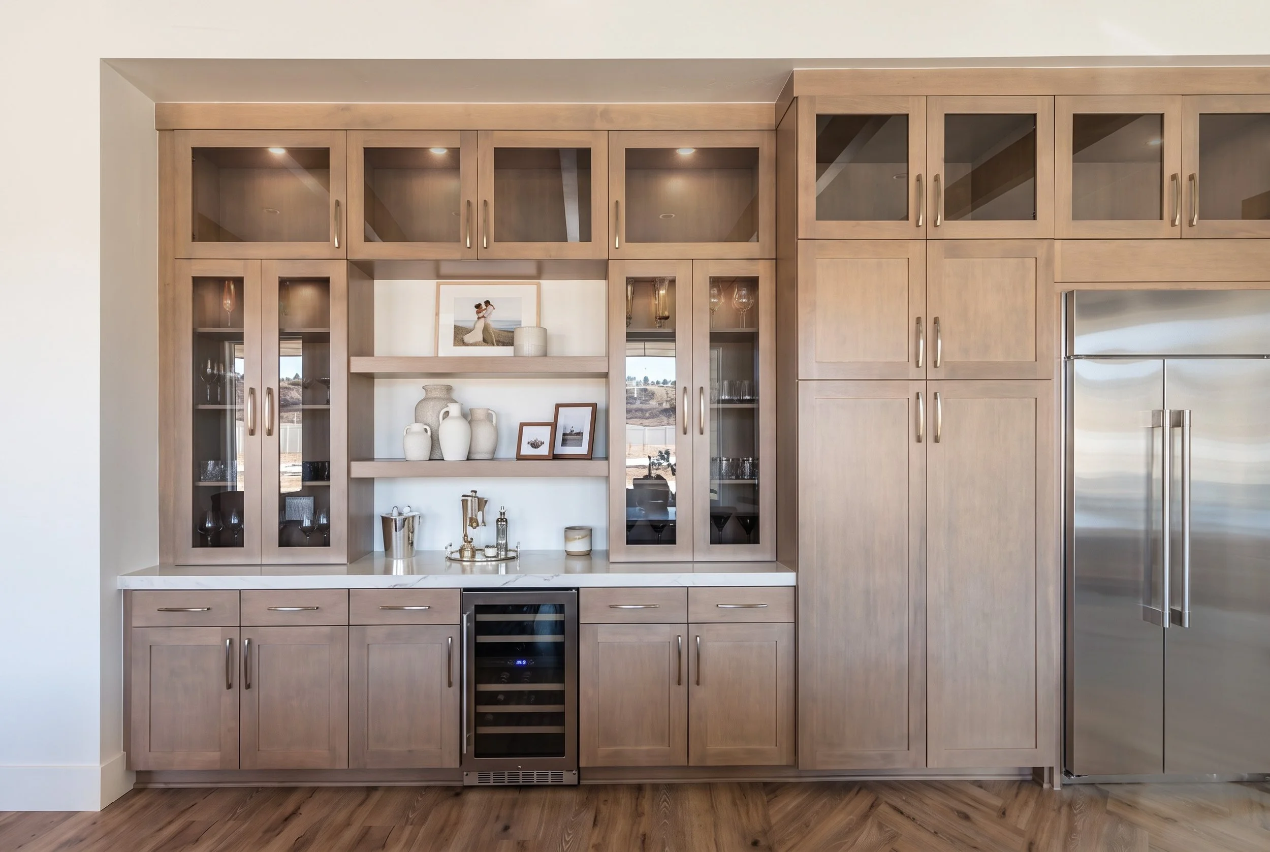 Bespoke kitchen extension home bar cabinetry with custom stain matching, upper glass display doors, integrated shelves, a built-in wine fridge, and stainless refrigerator.