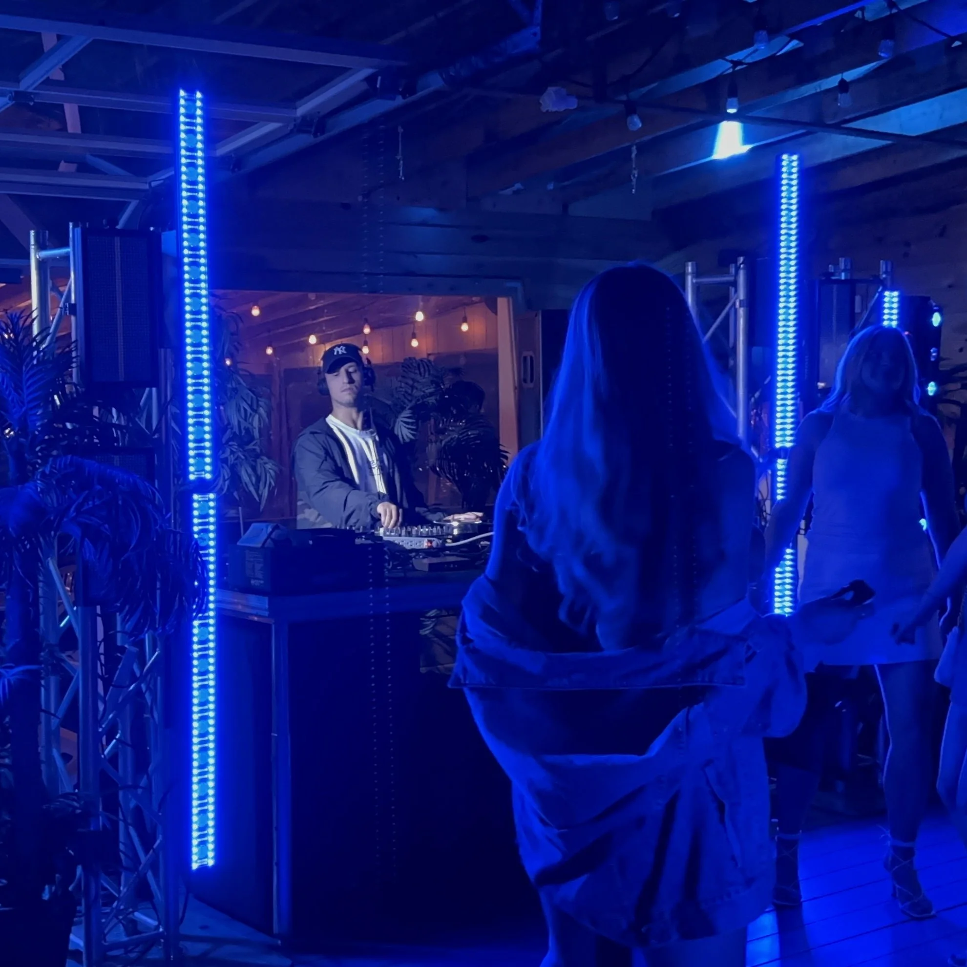 People dancing at a nightclub with a DJ in the background, illuminated by blue LED lights.