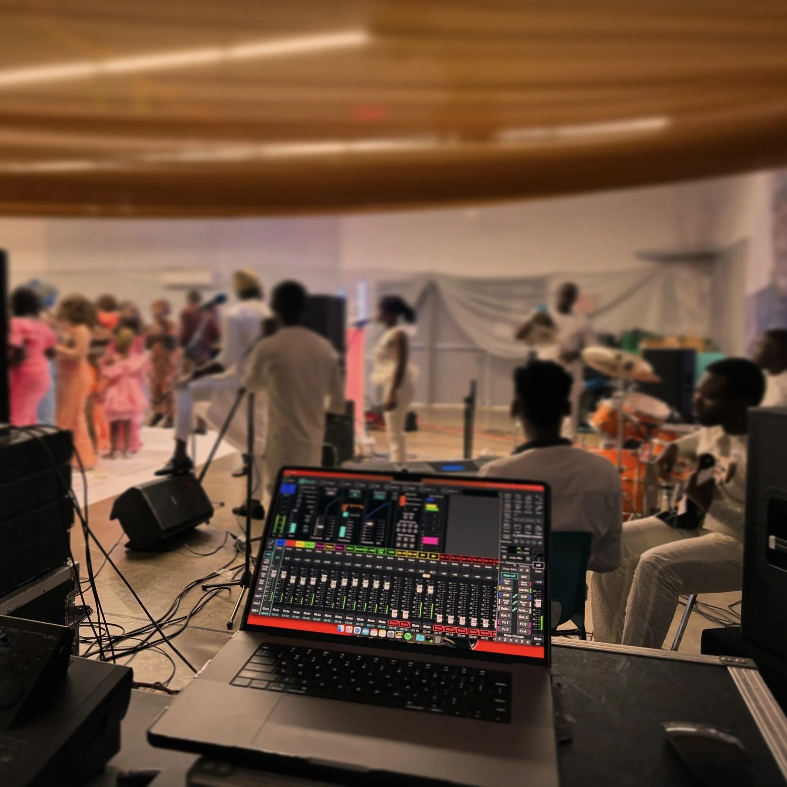 View of a stage performance with children and musicians, and a DJ mixing station in the foreground.