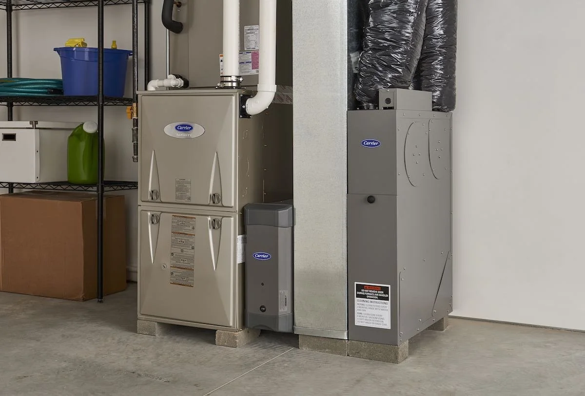 HVAC system with Carrier brand furnace, air handler, and ductwork in a utility room, with shelving and storage items in the background.
