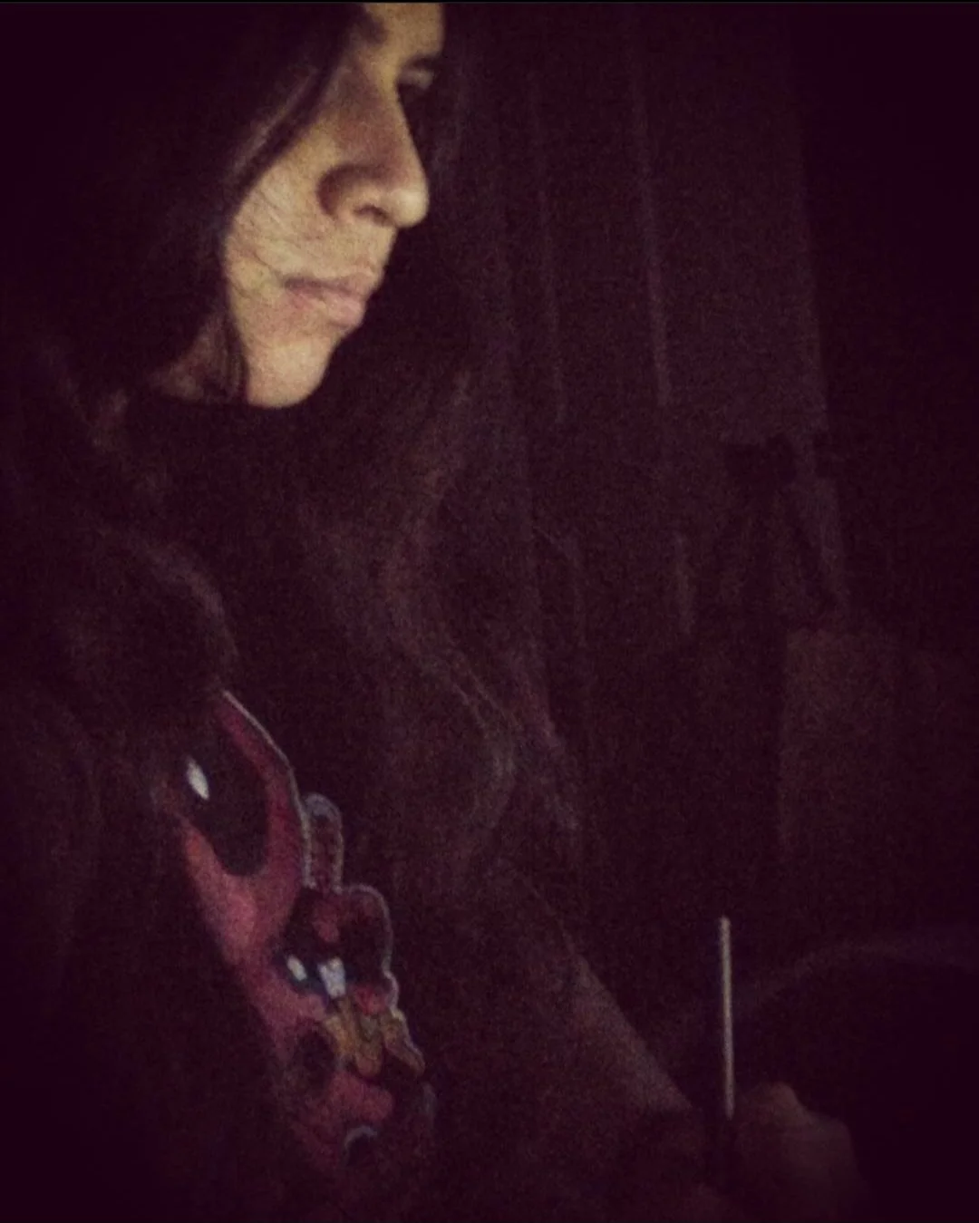 A woman with long dark hair in a dark environment, looking down, with a faint glow illuminating her face from her laptop as she writes.
