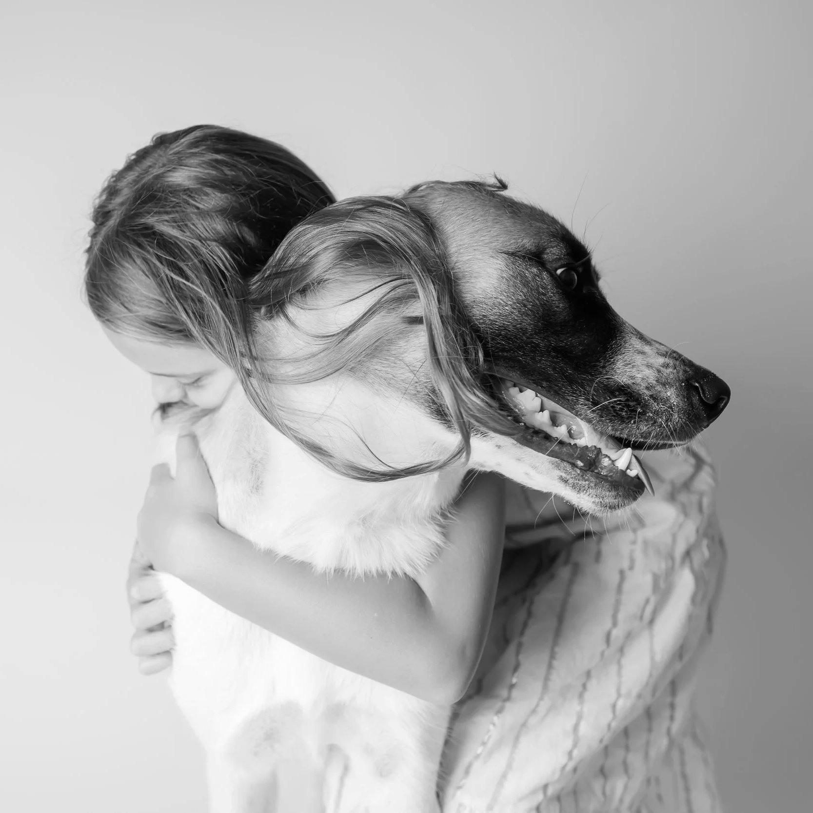A young girl hugging an Anatolian Shepherd puppy in a black and white photo.