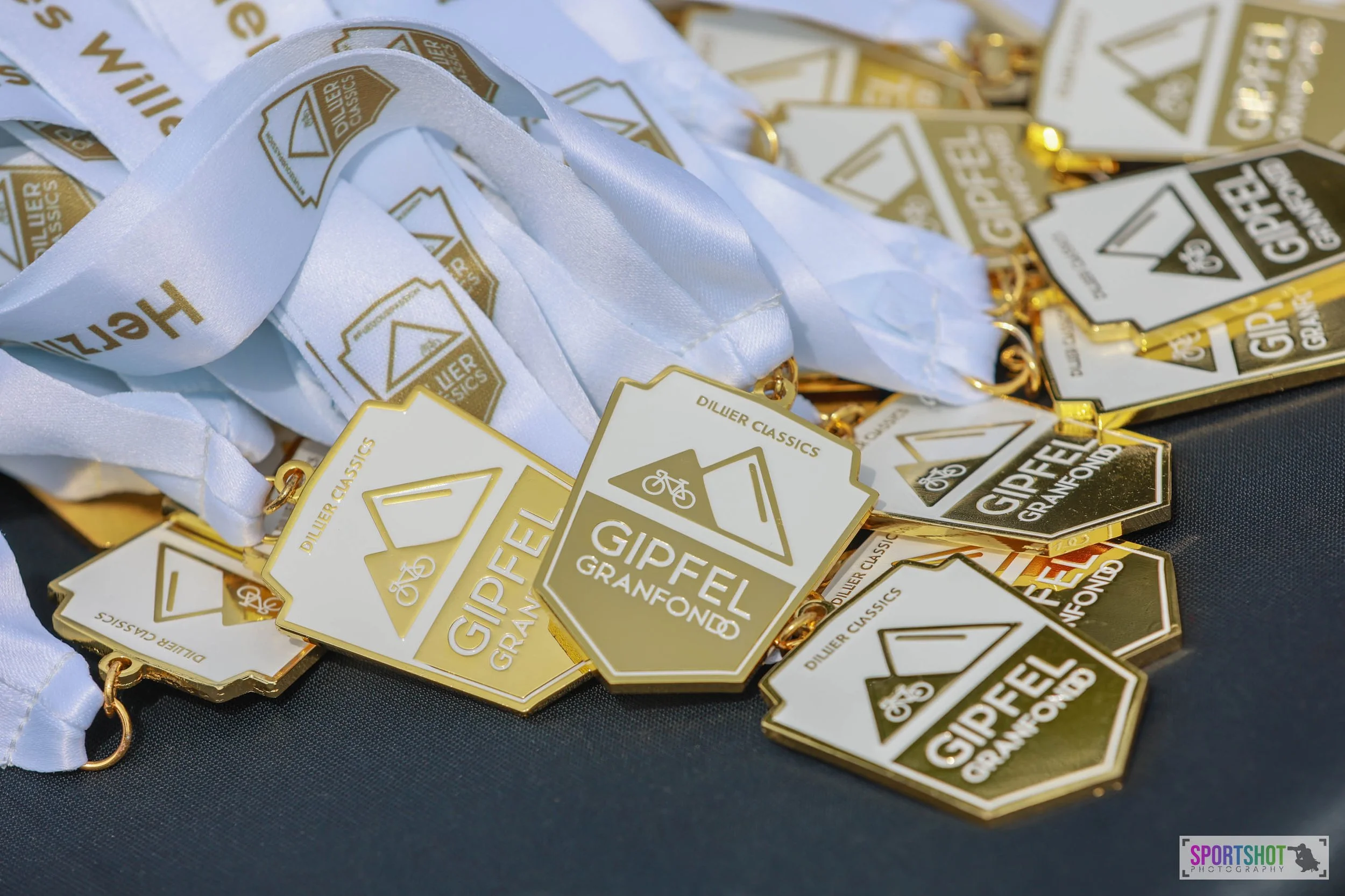 Stapel von Medaillen mit der Aufschrift "GIPFEL GRANFONDO" und "DILIER CLASSICS" auf weißen Bändern.
