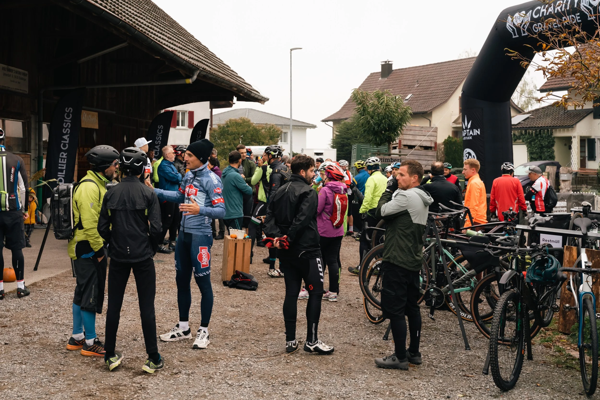 Menschen, die in Fahrradkleidung bei einer Veranstaltung im Freien stehen, mit Fahrrädern und einem aufblasbaren Torbogen im Hintergrund.