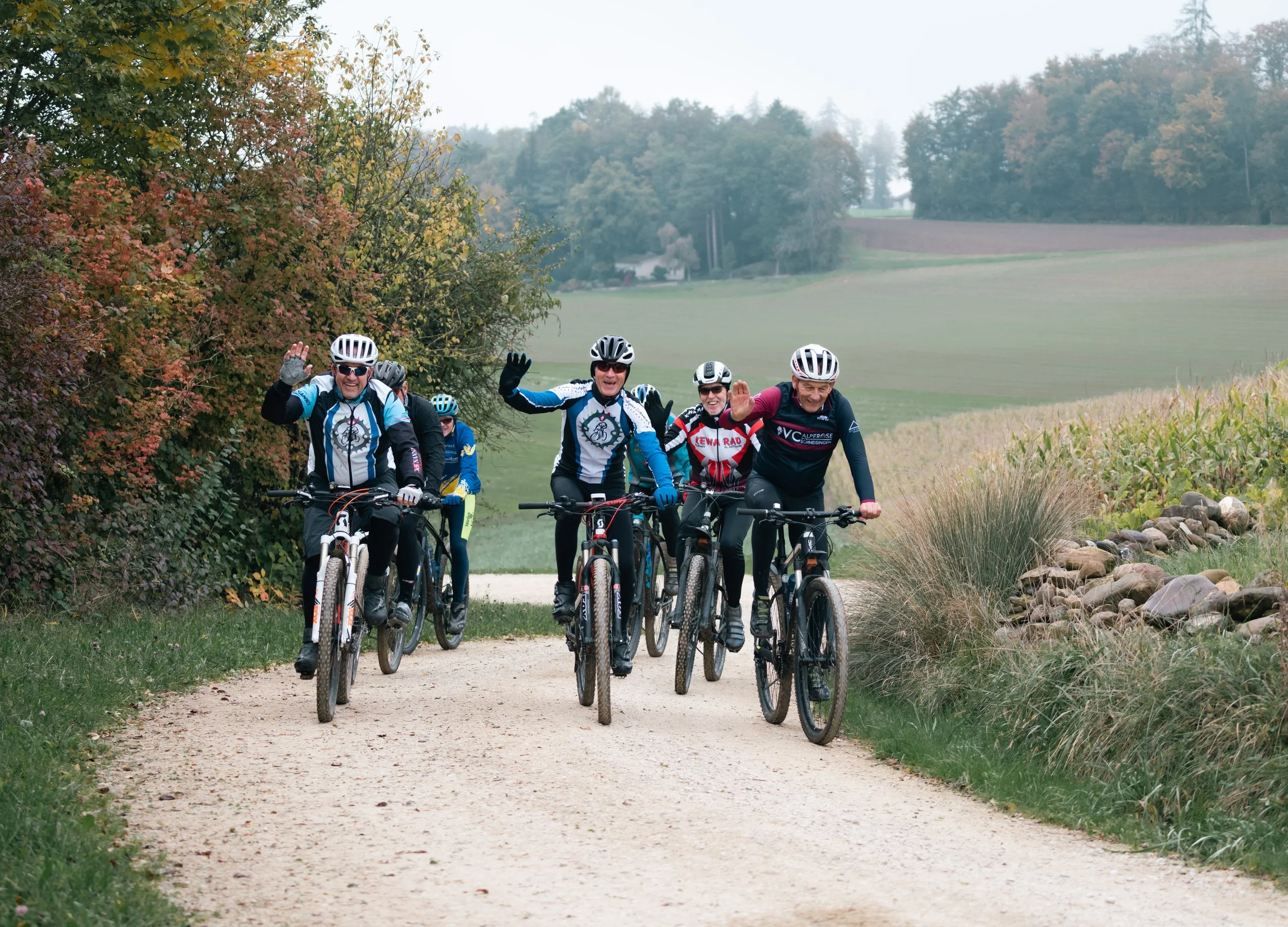 Gruppe von Radfahrern auf einem Schotterweg in einer ländlichen Landschaft, umgeben von Bäumen im Herbst.