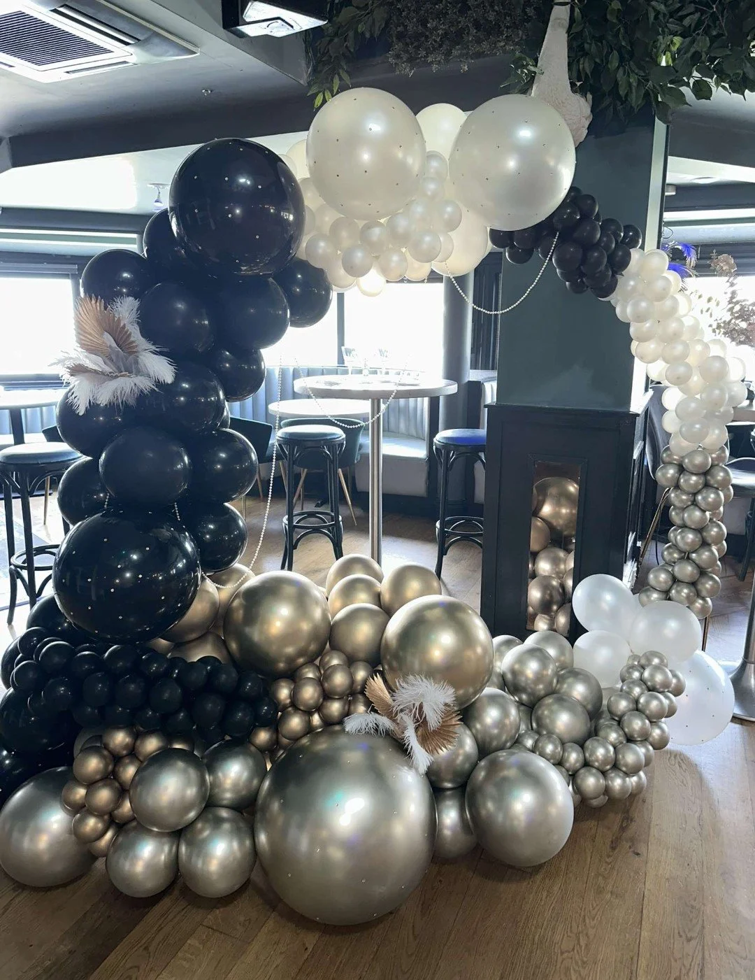 Decorative balloon arch with black, white, and metallic gold balloons in a modern indoor setting.