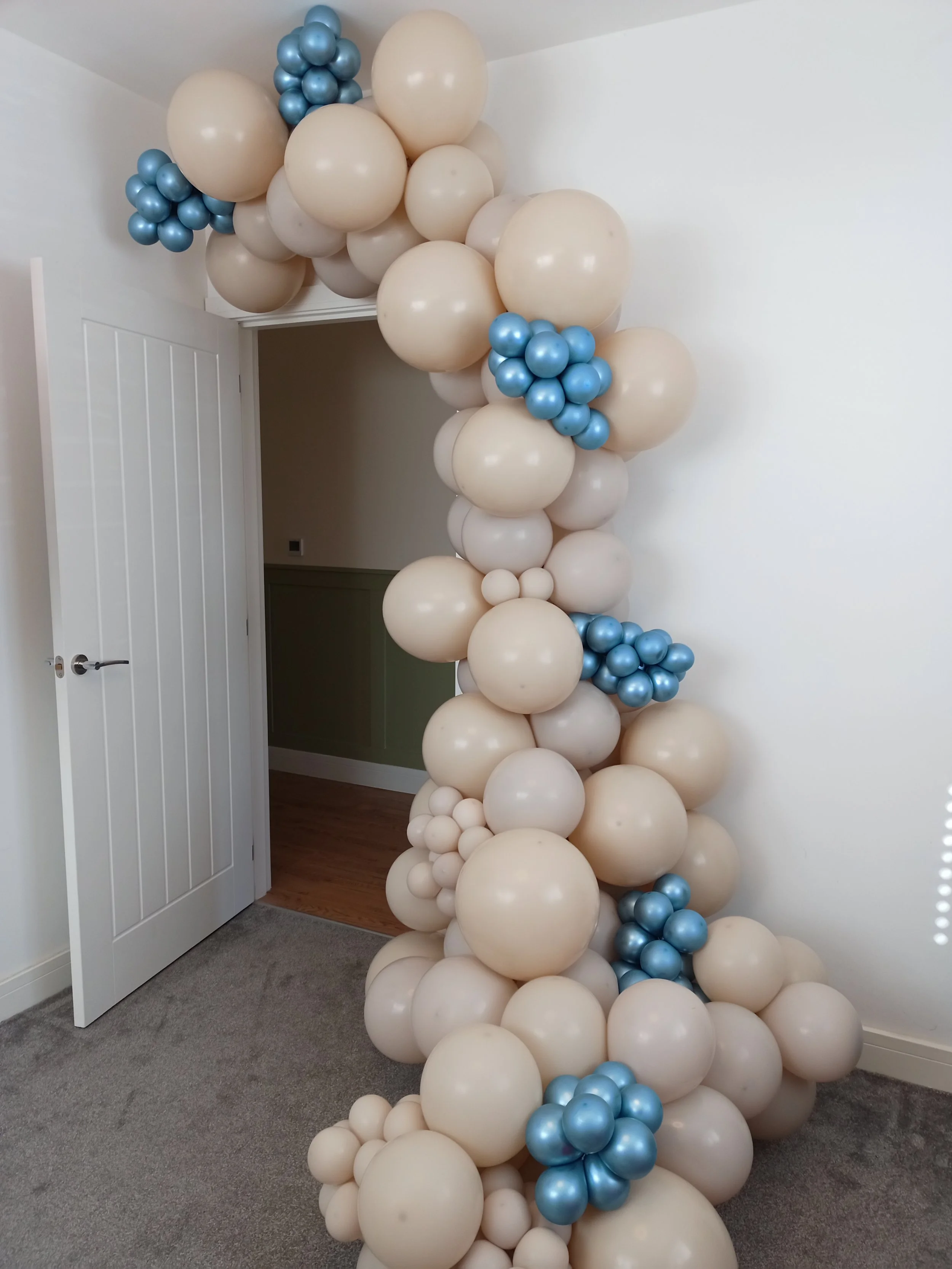 A decorative arrangement of beige and light blue balloons forming an arch or column next to a door in a room.