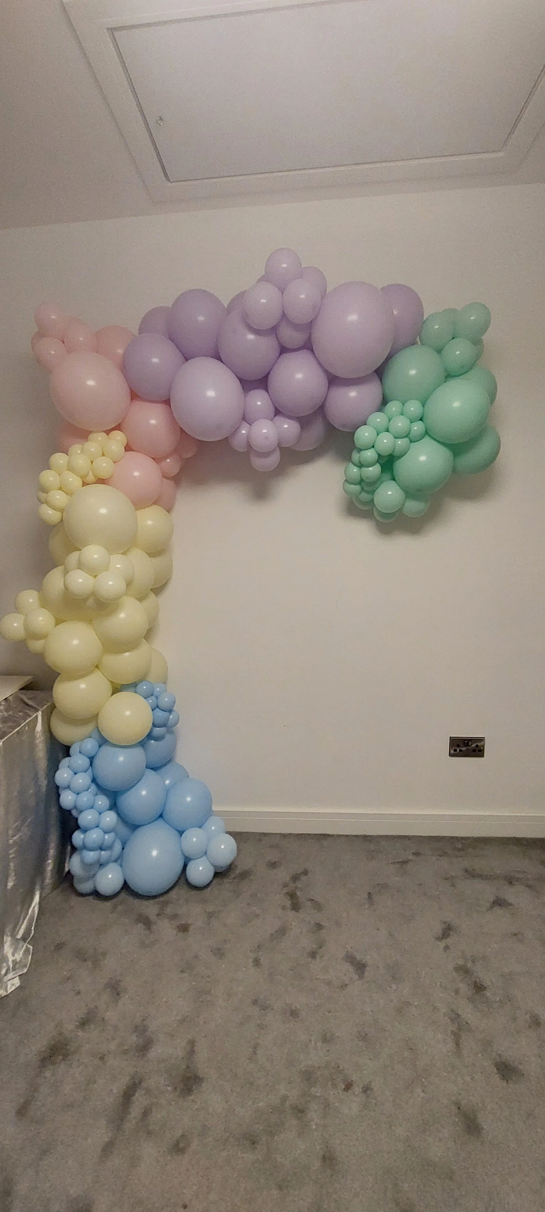 Colorful balloon arrangement on a wall with pastel purple, green, yellow, and blue balloons forming a decorative pattern.