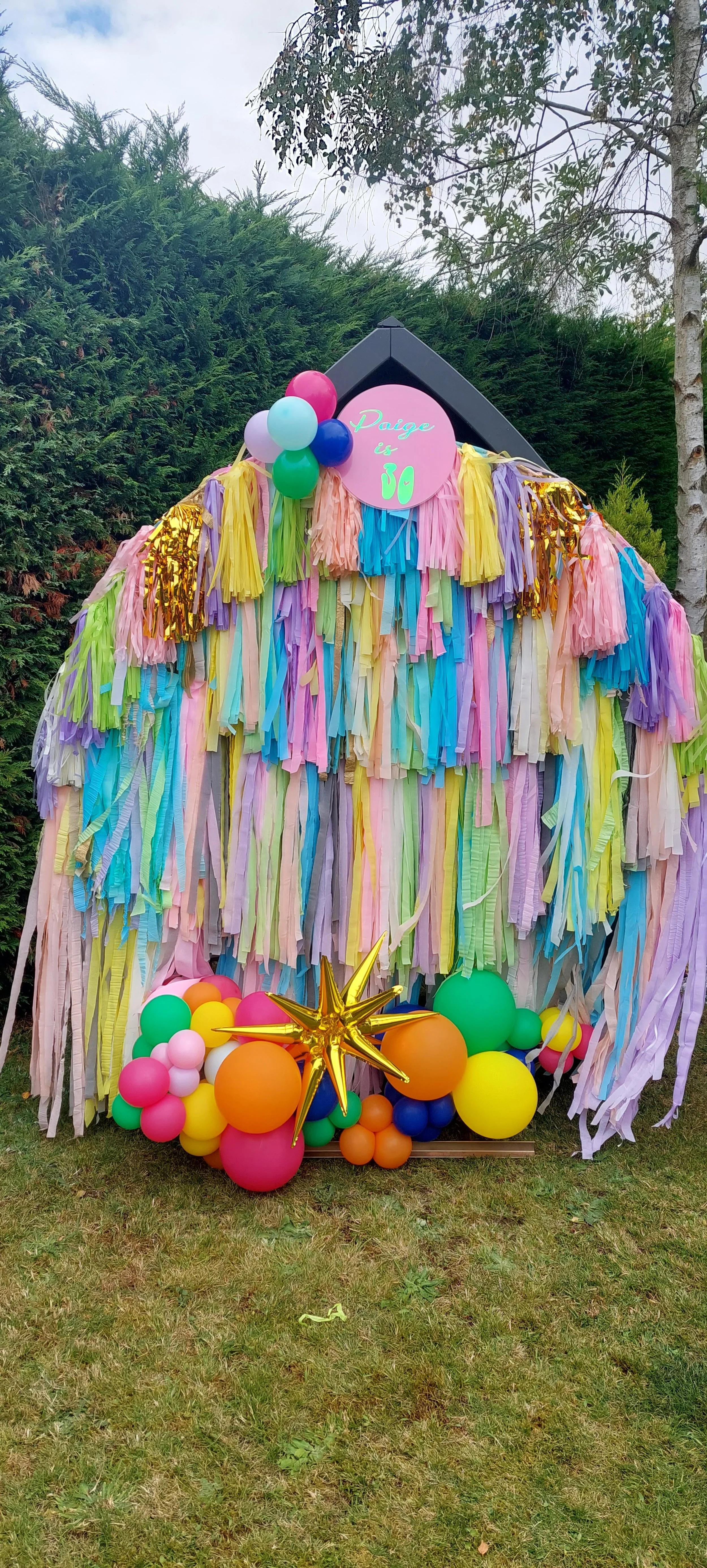 Colorful birthday party decoration with rainbow-colored streamers, balloons, and a sign that reads "Paige is 30."