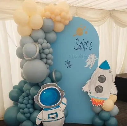 Decorative display with balloons in shades of blue, white, and beige, featuring a space theme with a rocket, astronaut, and planets, and the word 'Saints' written on a large blue semicircular backdrop.