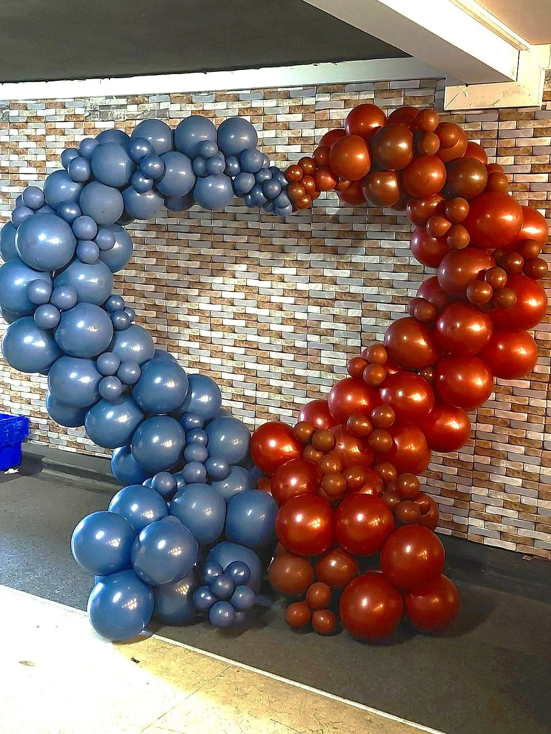 A balloon display with blue and red balloons arranged in circle shapes against a brick wall background.