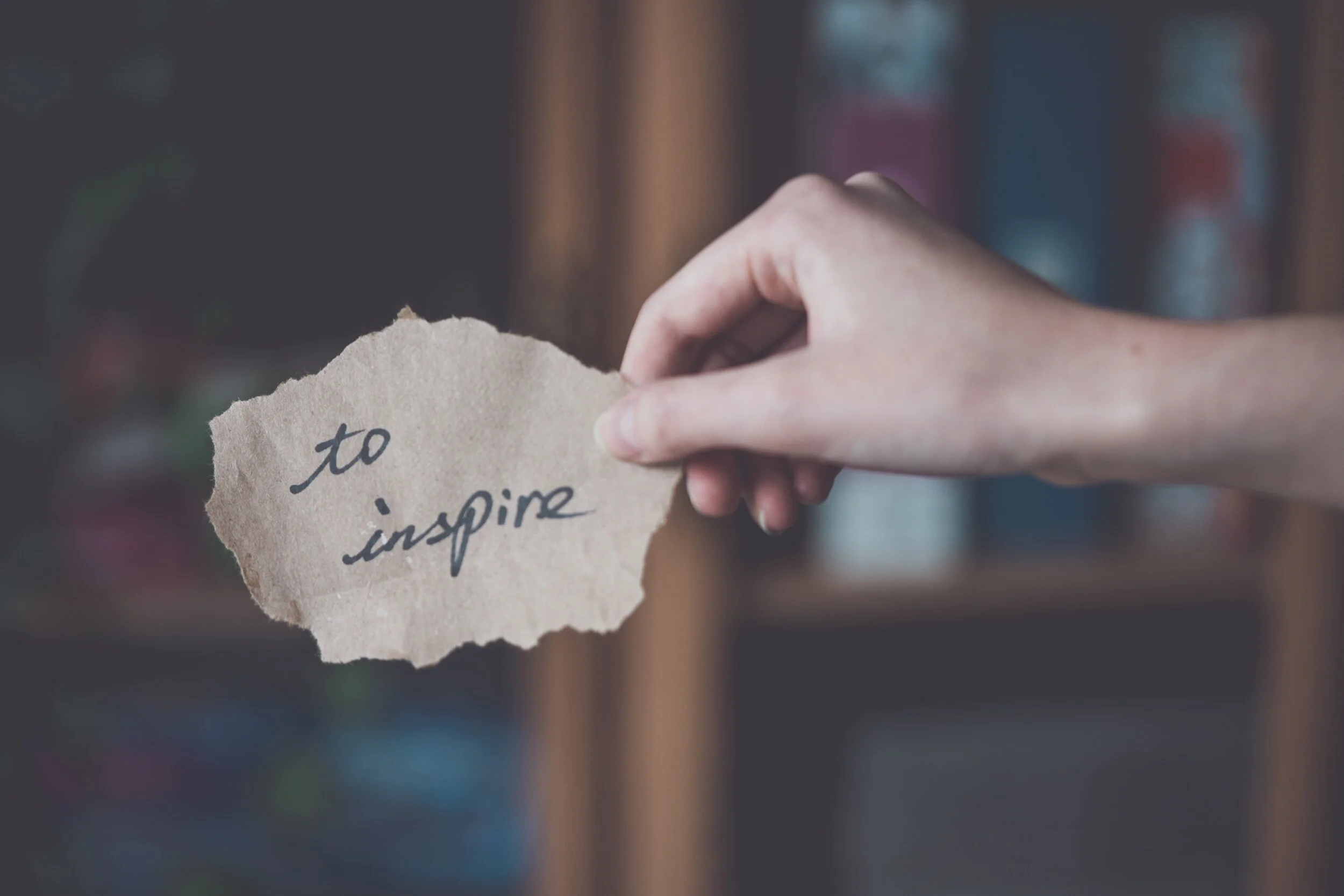 right hand holding note with writing "To inspire"