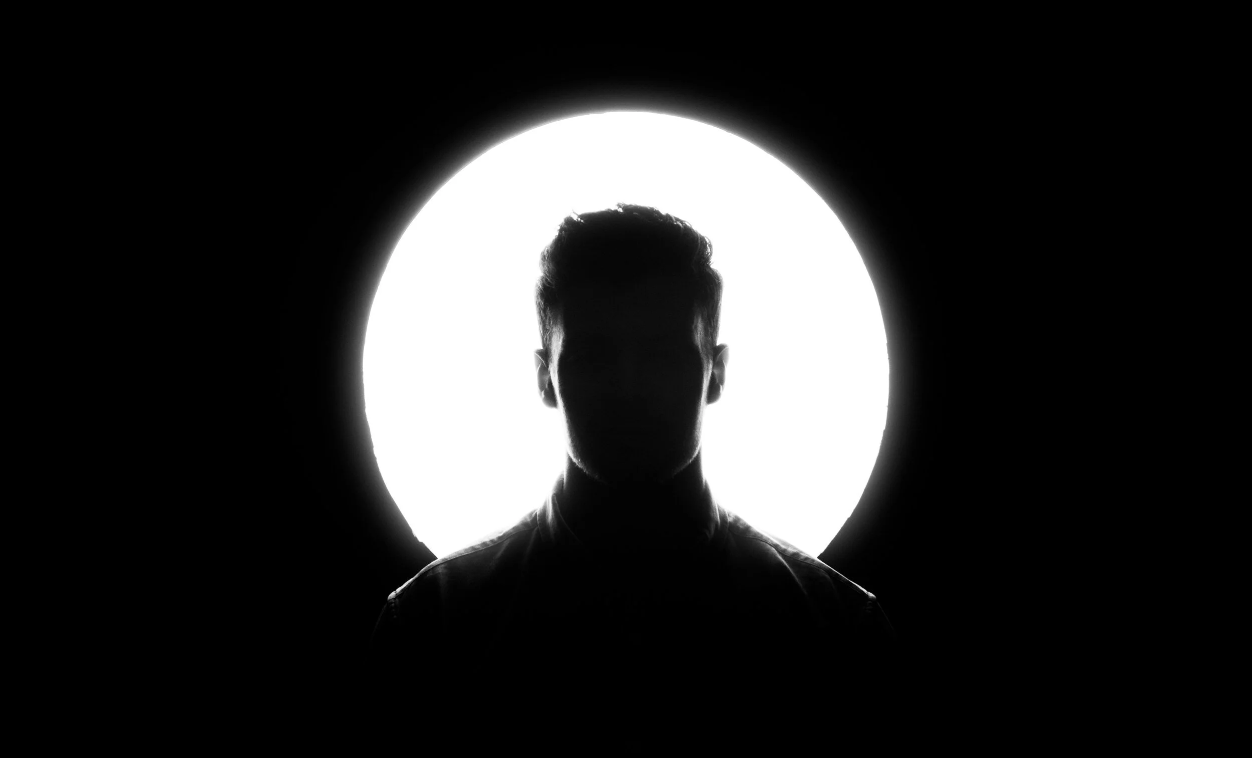 Silhouette of a person with short hair against a bright circular light in a dark room.