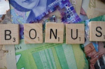 Scrabble letter tiles spell bonus on a background of brightly coloured banknotes.