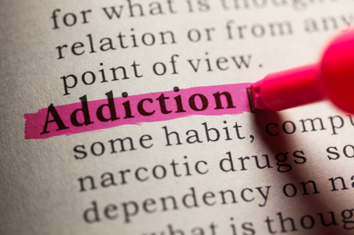 Close-up of a dictionary page with the word 'Addiction' highlighted in pink and a pink highlighter pen nearby.