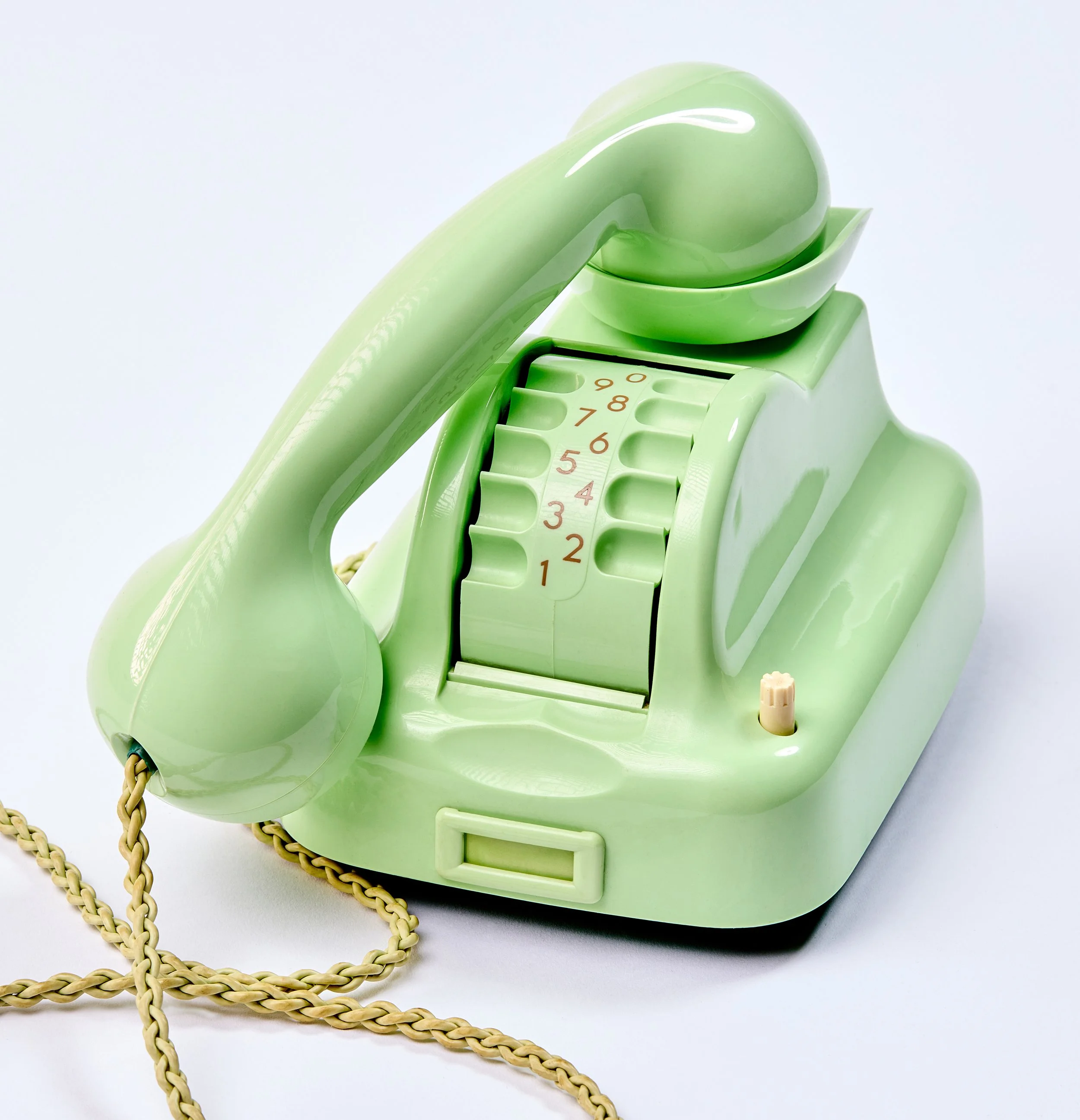 Ein grüner, vintage Drehtelefon, Trommelwähler,  mit Schnur und Zifferblatt gegen einen weißen Hintergrund.