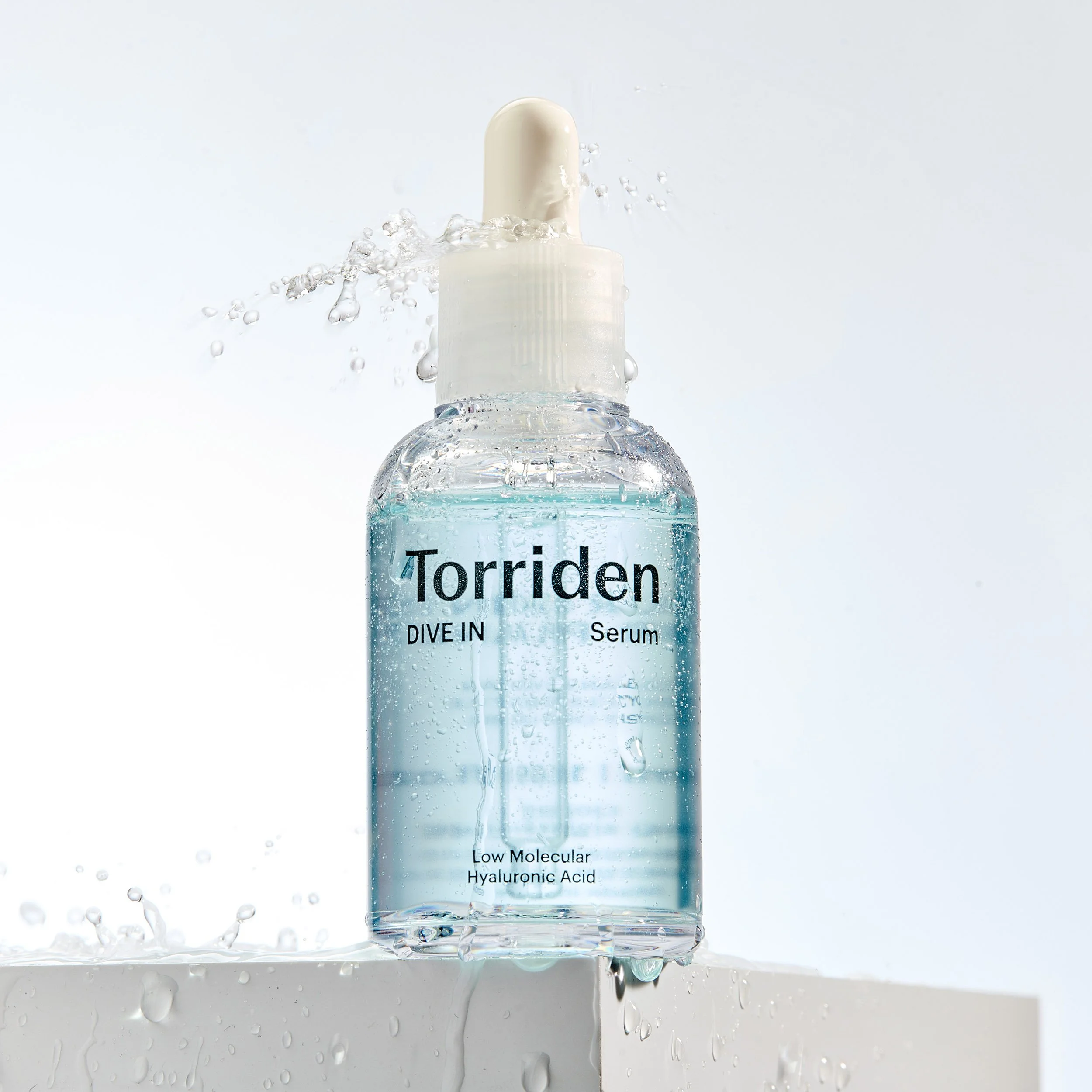 Flasche mit Wasser und Produktetikett, Wasser spritzt, Text auf Flasche lautet 'Torriden Dive In Serum', enthält Hyaluronsäure, niedrige Molekulargröße.