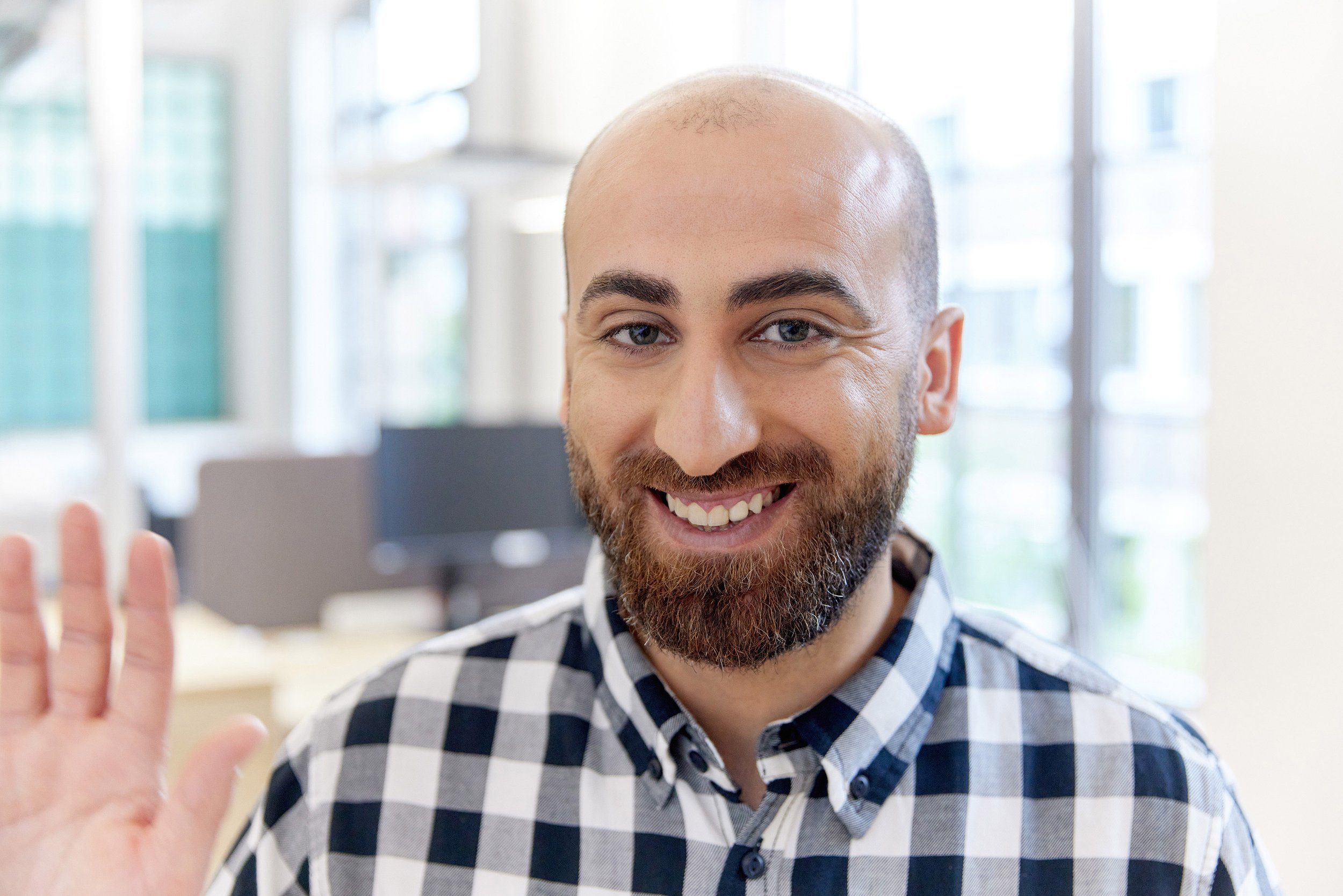 modernes Mitarbeiterfoto, junger Mann winkt freundlich zur Kamera