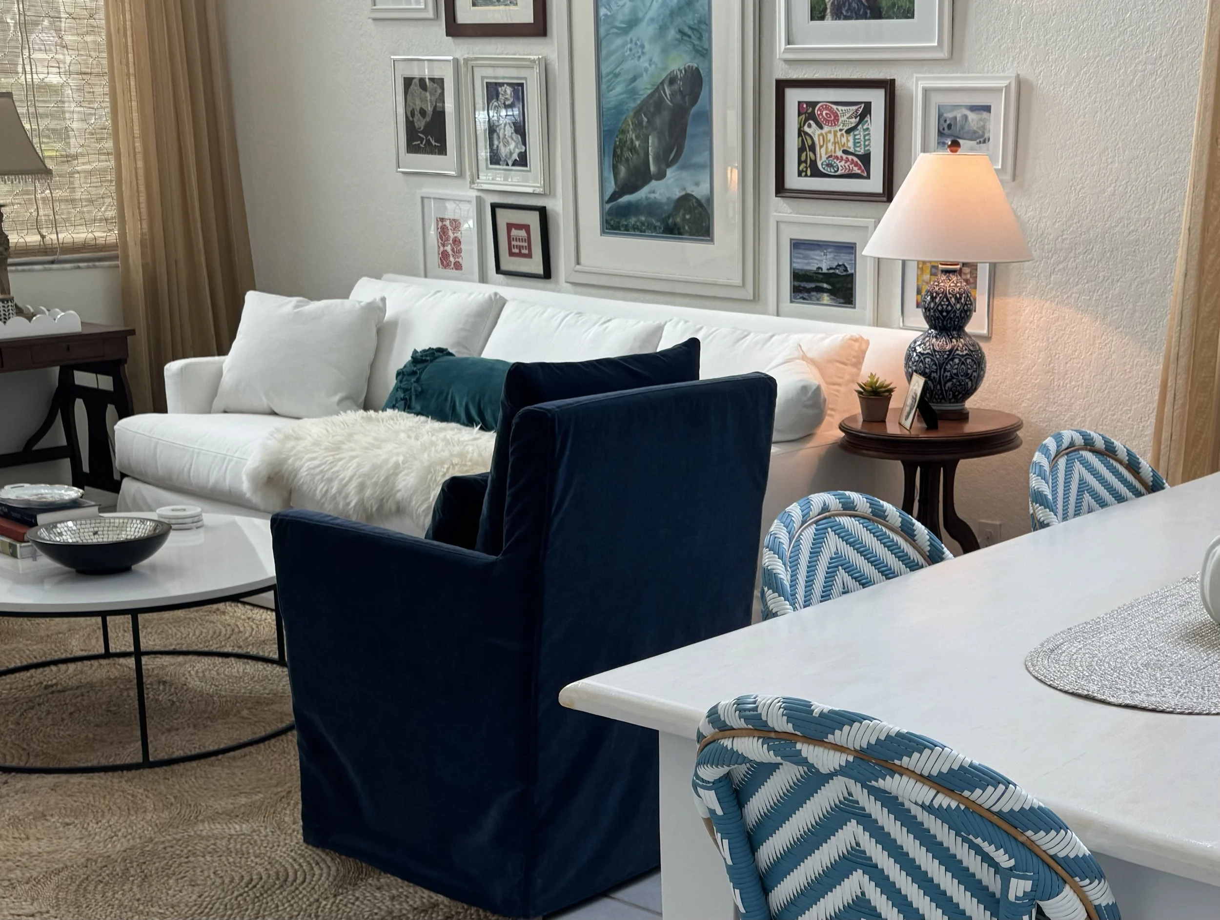 Living room with a white sofa, blue armchair, glass coffee table, wall art, and a table lamp with a decorative base.