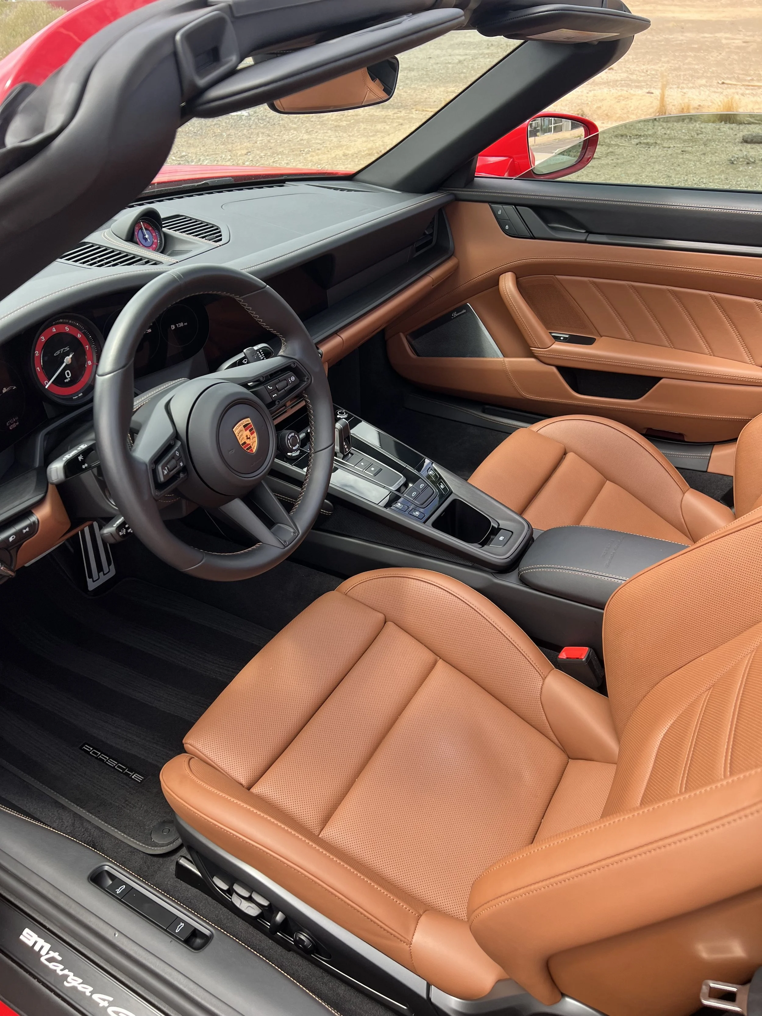 Interior of a Porsche sports car with tan leather seats, black and gray dashboard, and sporty instrumentation.