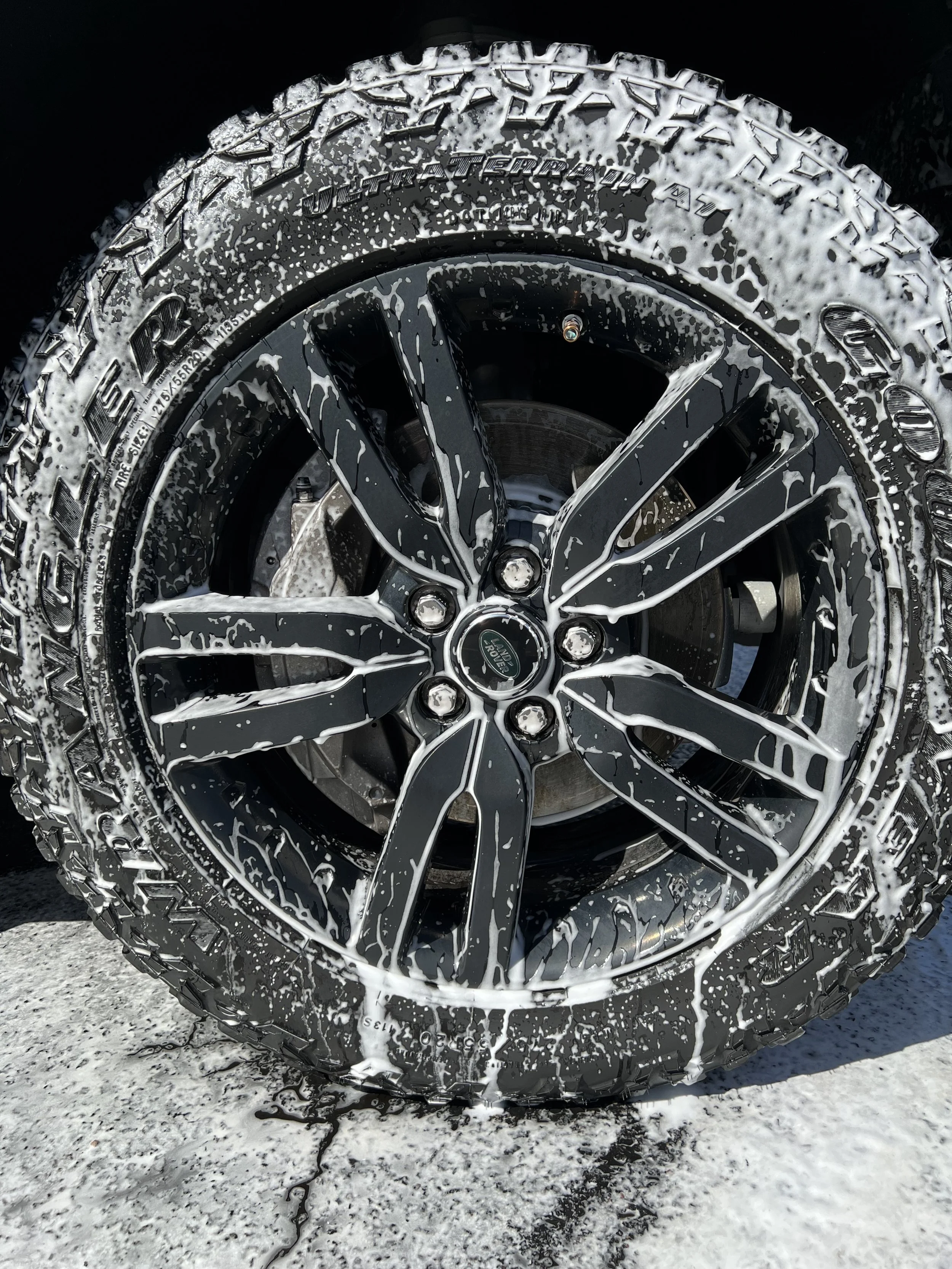 Car tire with foam soap and water for washing, on a gray concrete surface.