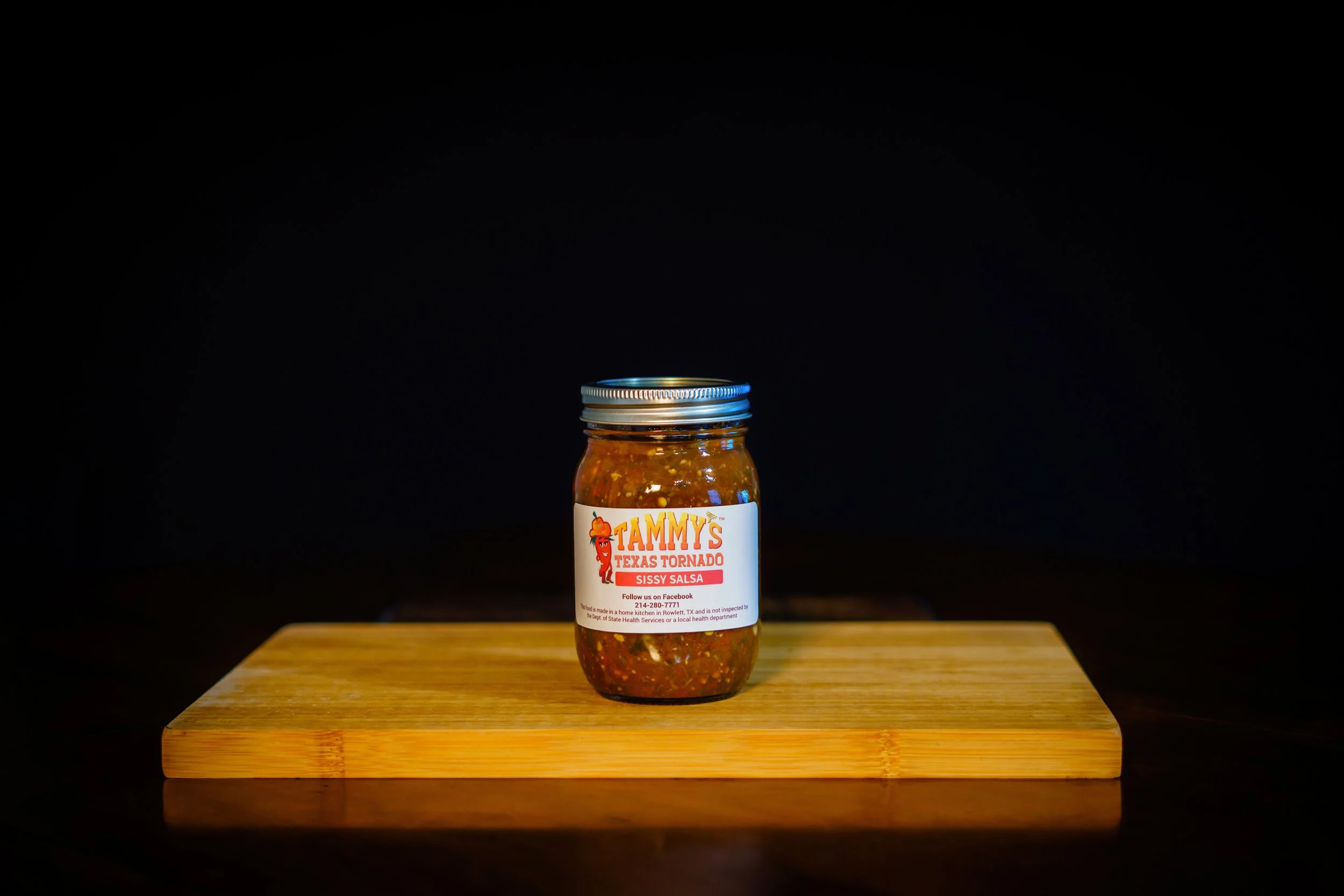 Jar of Tammy's Texas Tornado Sissy Salsa on a wooden surface with a black background.