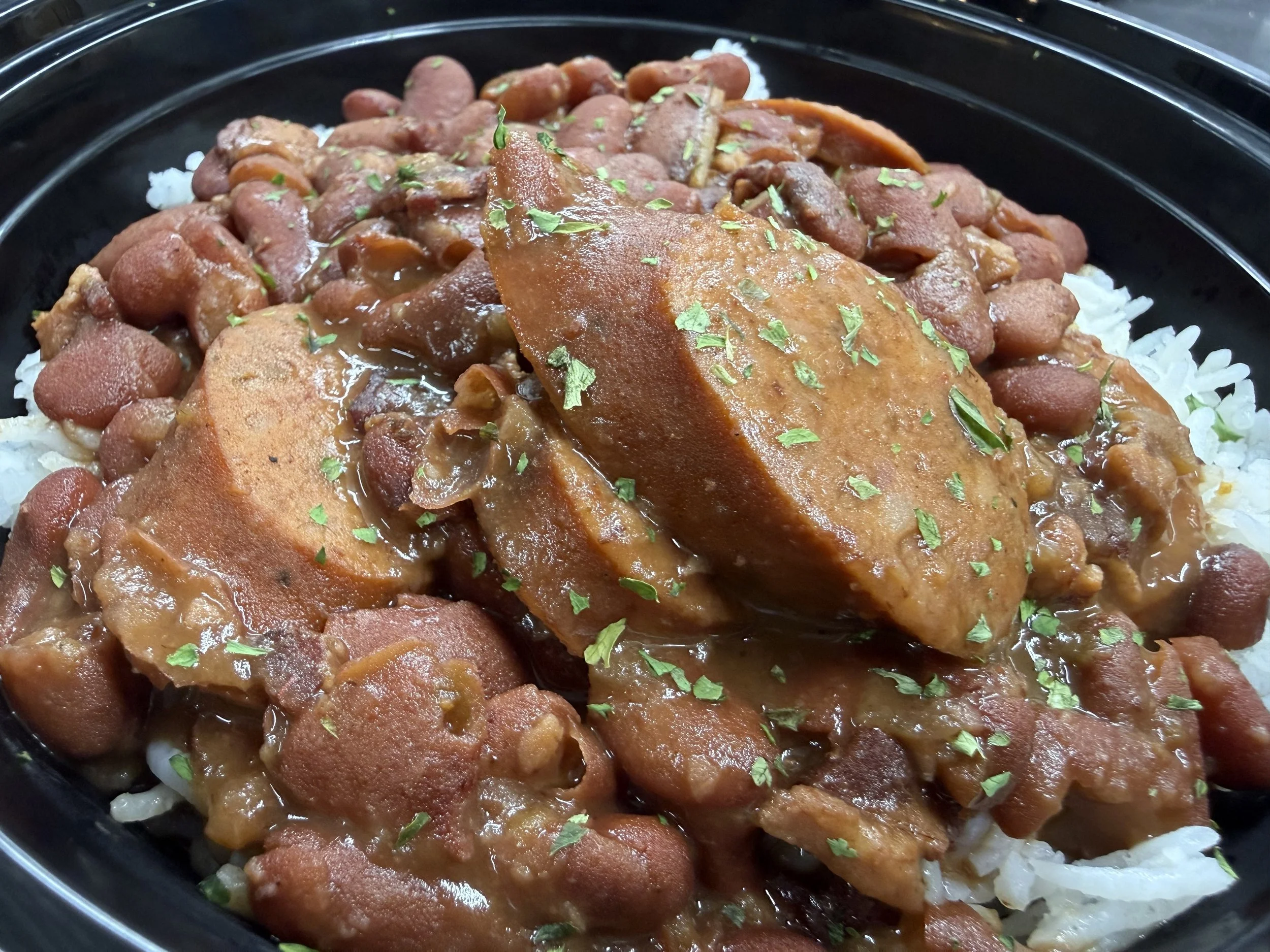 A close-up of a dish with white rice topped with a brown meat stew, garnished with chopped green herbs.