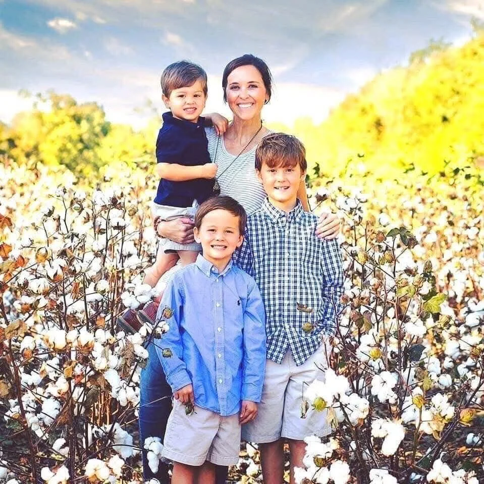 A woman with four young boys standing in a cotton field during daytime, smiling at the camera.