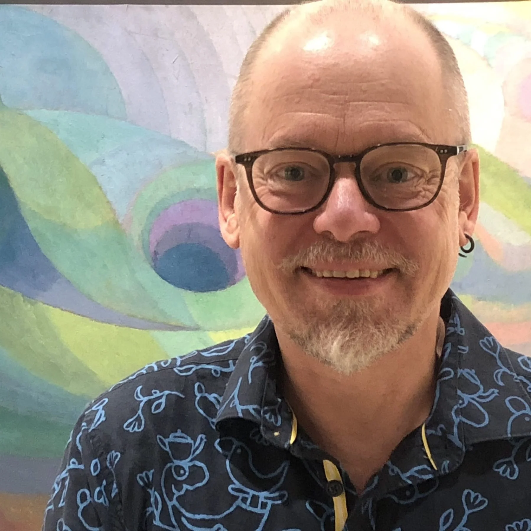 A photo of Kirk Patston speaker at Build 2026 Conference, he is smiling with glasses and an earring in front of an abstract colorful mural.